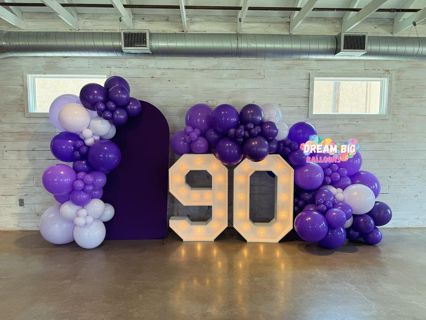 A room filled with purple and white balloons and a sign that says 90.