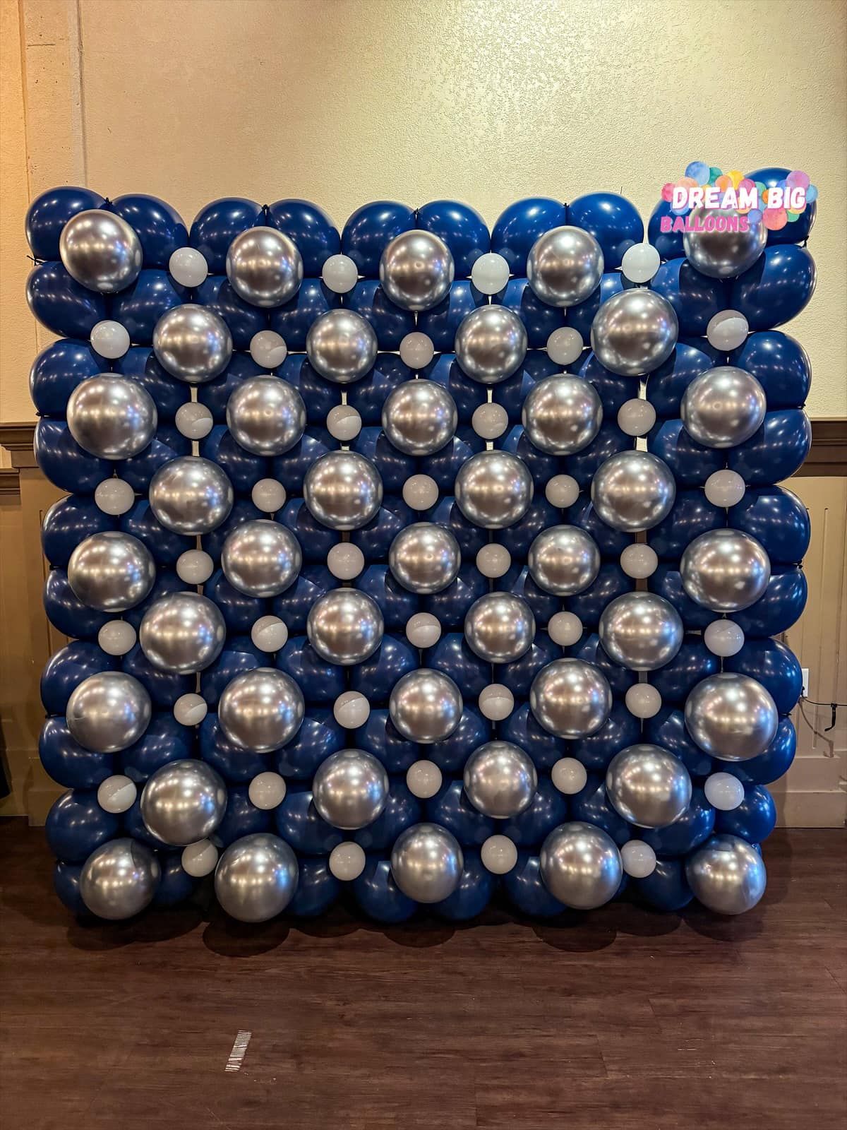 a wall made of blue and silver balloons on a wooden floor