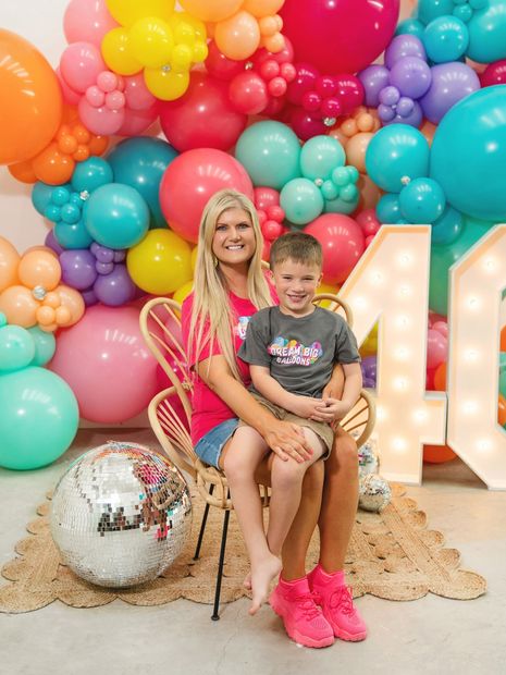 A woman is standing in front of a wall filled with colorful balloons.