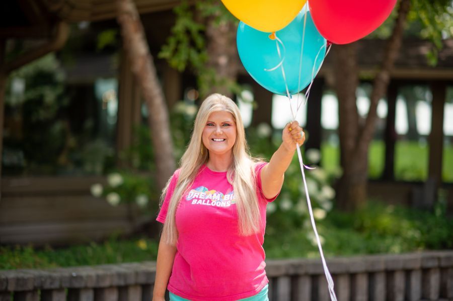 A woman in a pink shirt is holding a bunch of colorful balloons.