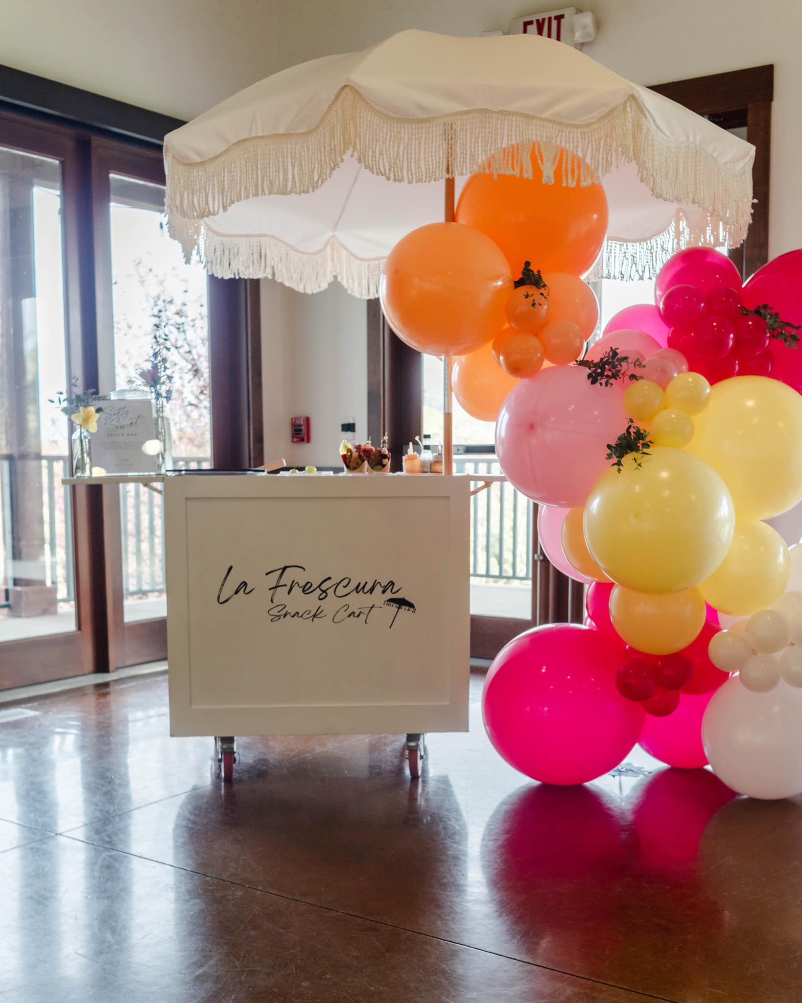 A white umbrella is surrounded by balloons in a room.