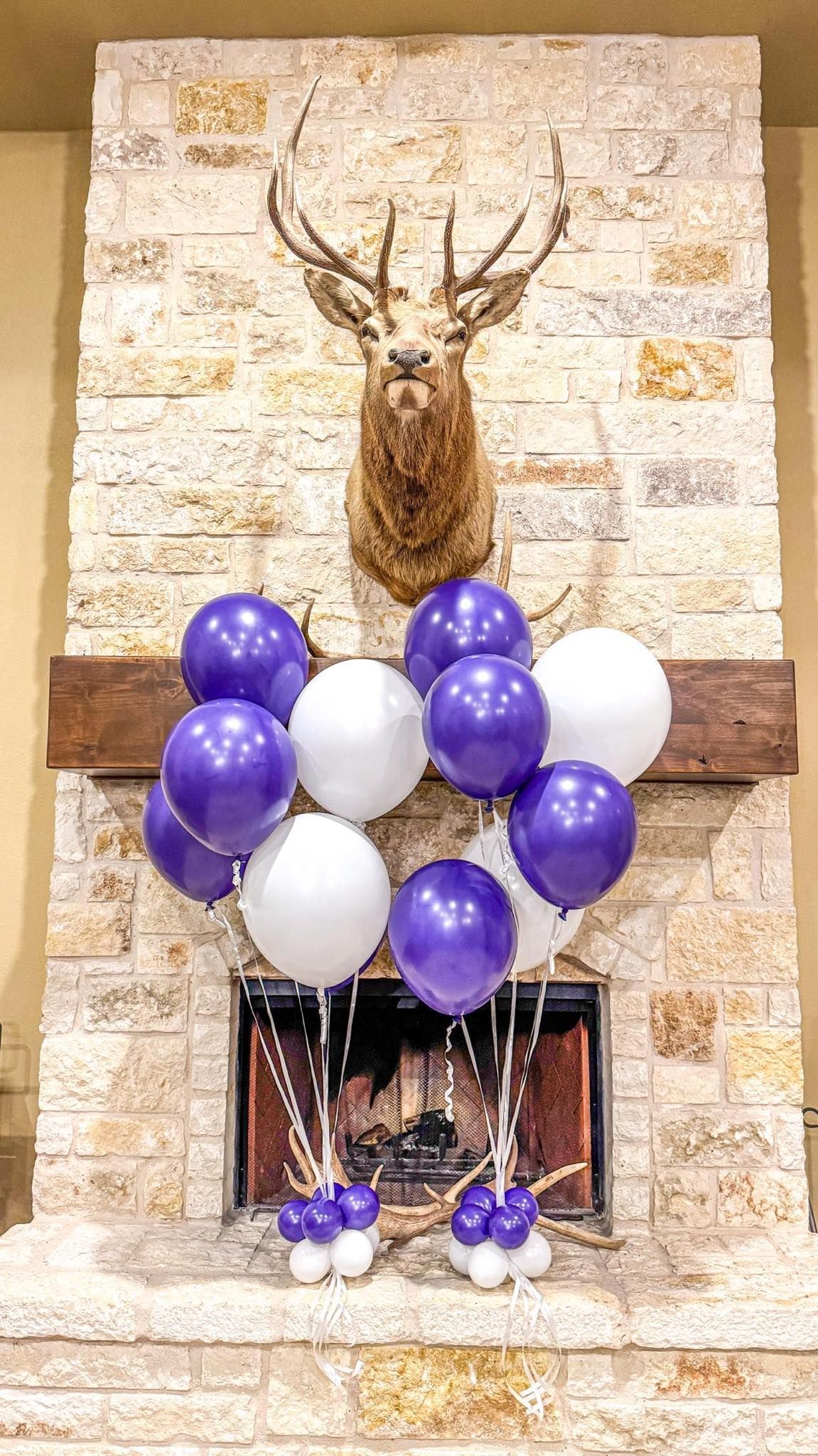 A fireplace decorated with purple and white balloons and a deer head.