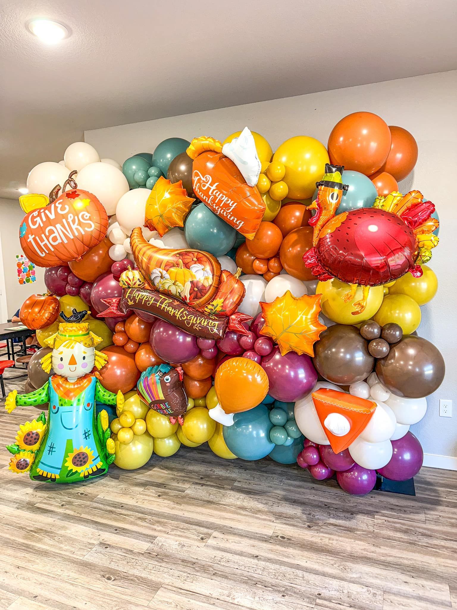 A wall filled with lots of balloons and a scarecrow.