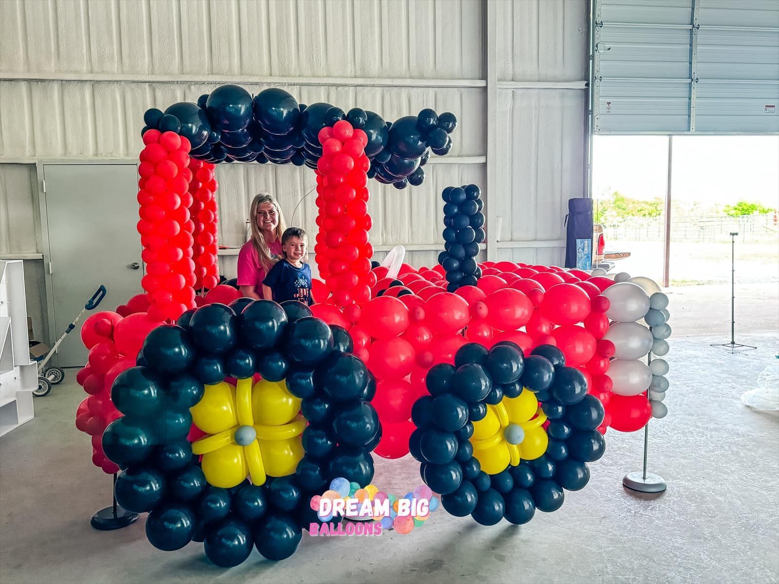 A woman and child are standing in front of a tractor made of balloons.