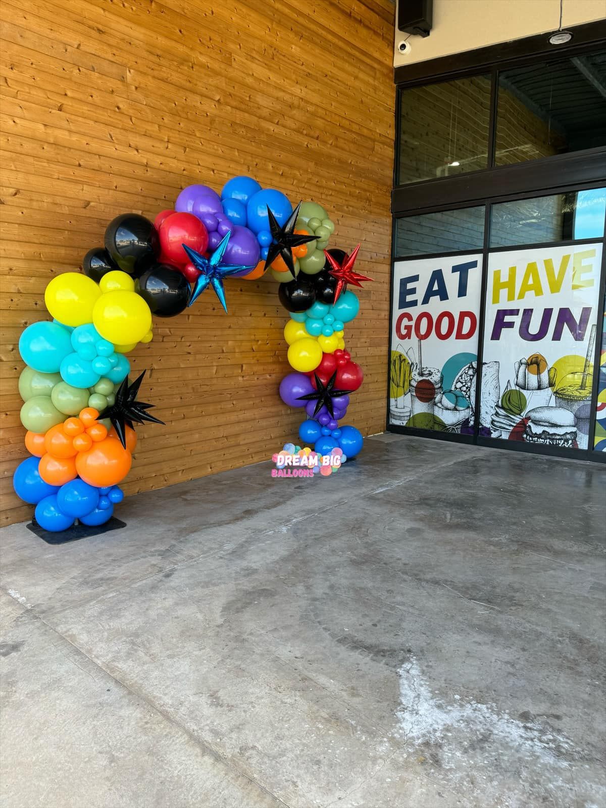 a colorful balloon arch is in front of a building that says eat have good fun