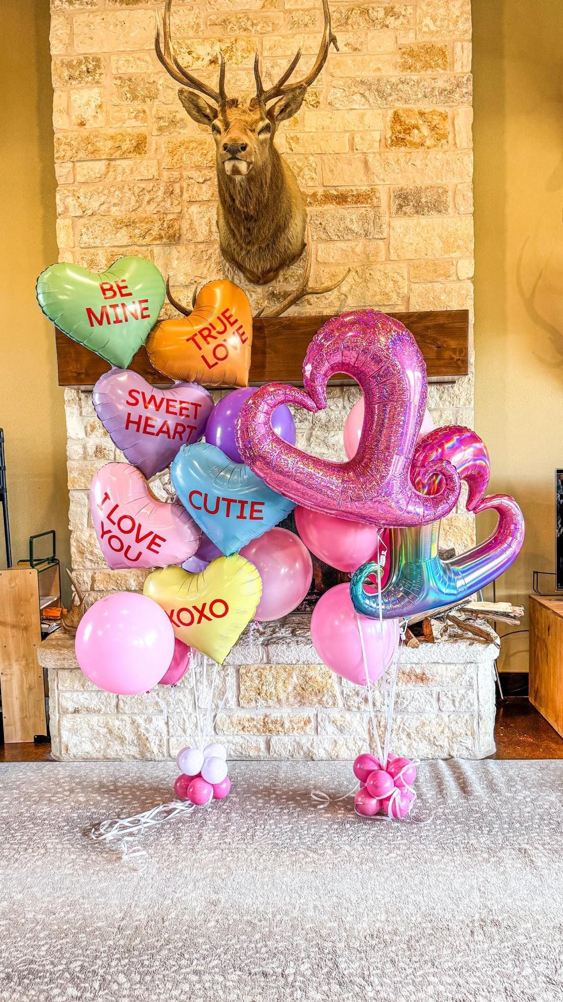 A bunch of balloons in the shape of hearts are sitting in front of a fireplace.
