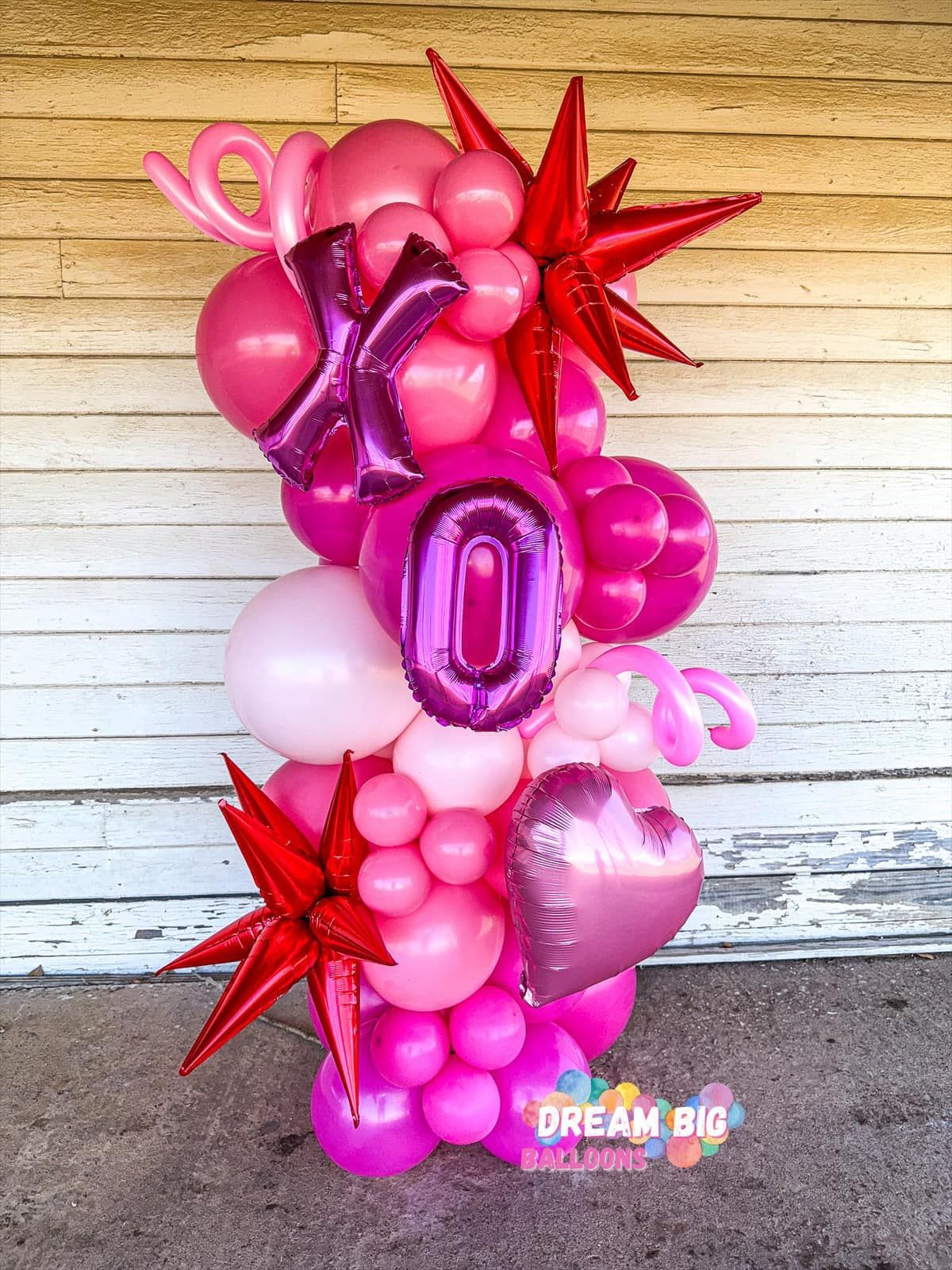 A bunch of pink and purple balloons are sitting in front of a wooden wall.