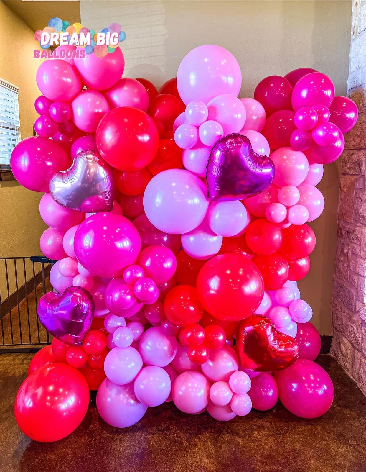 A wall of pink and red balloons with hearts on them.