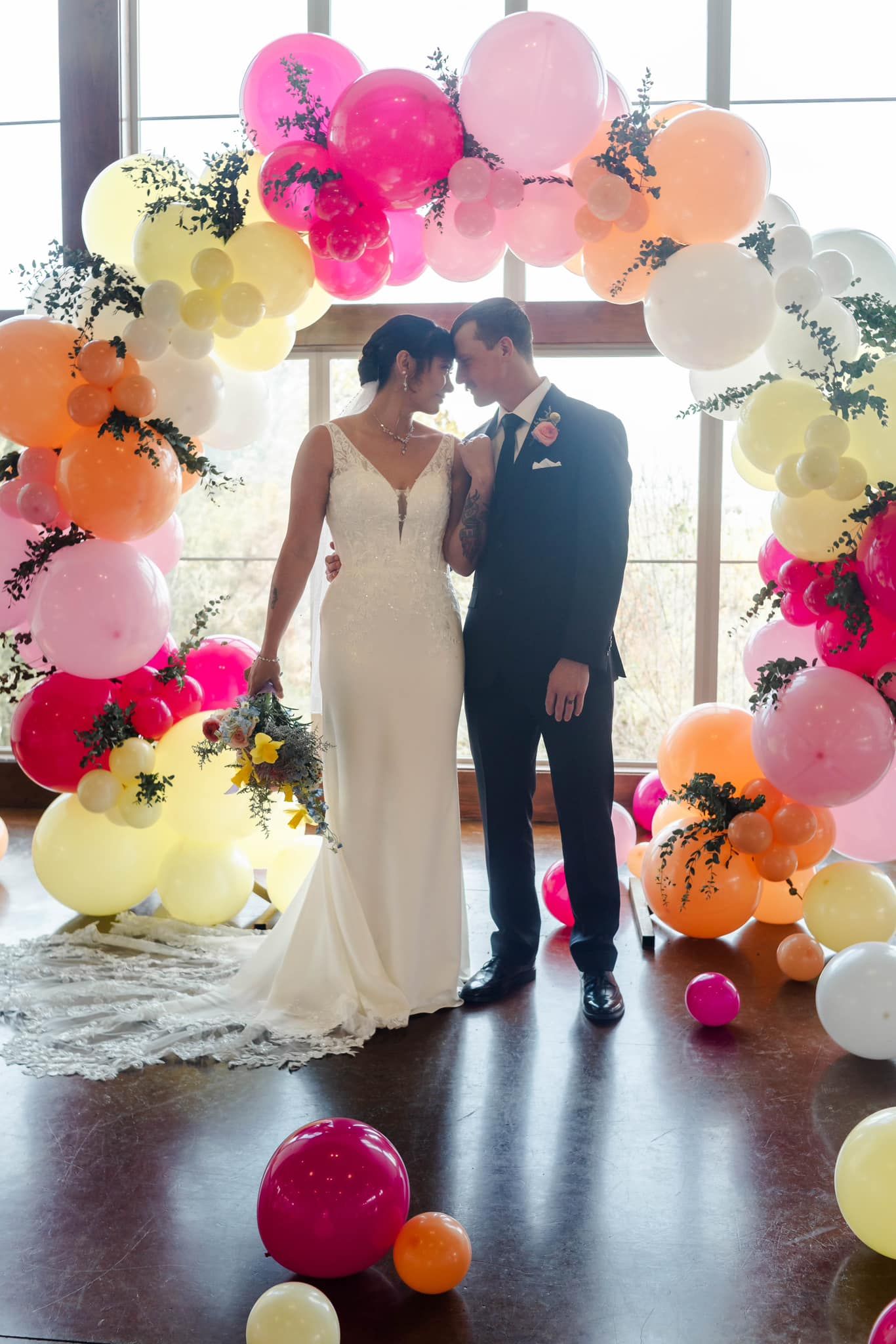 A bride and groom are standing under a balloon arch.