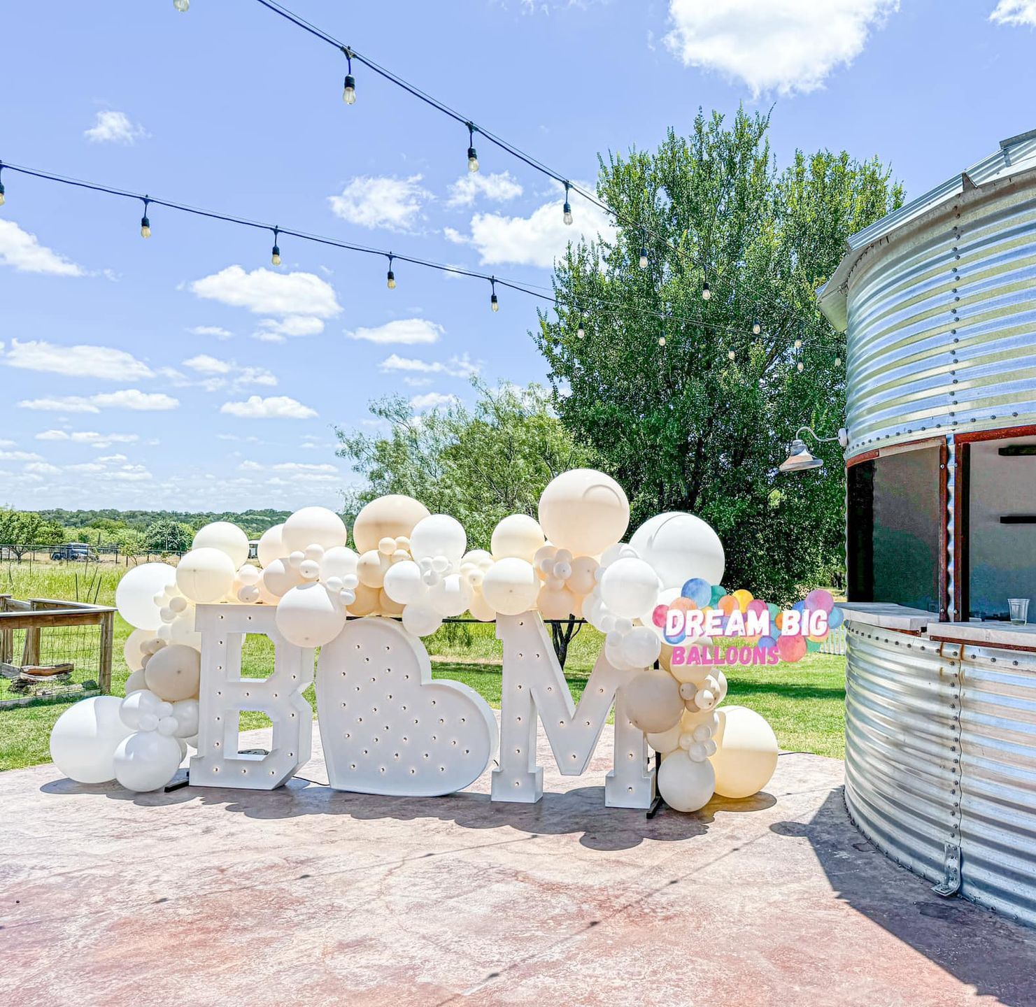 A large sign made of balloons is sitting in front of a silo.