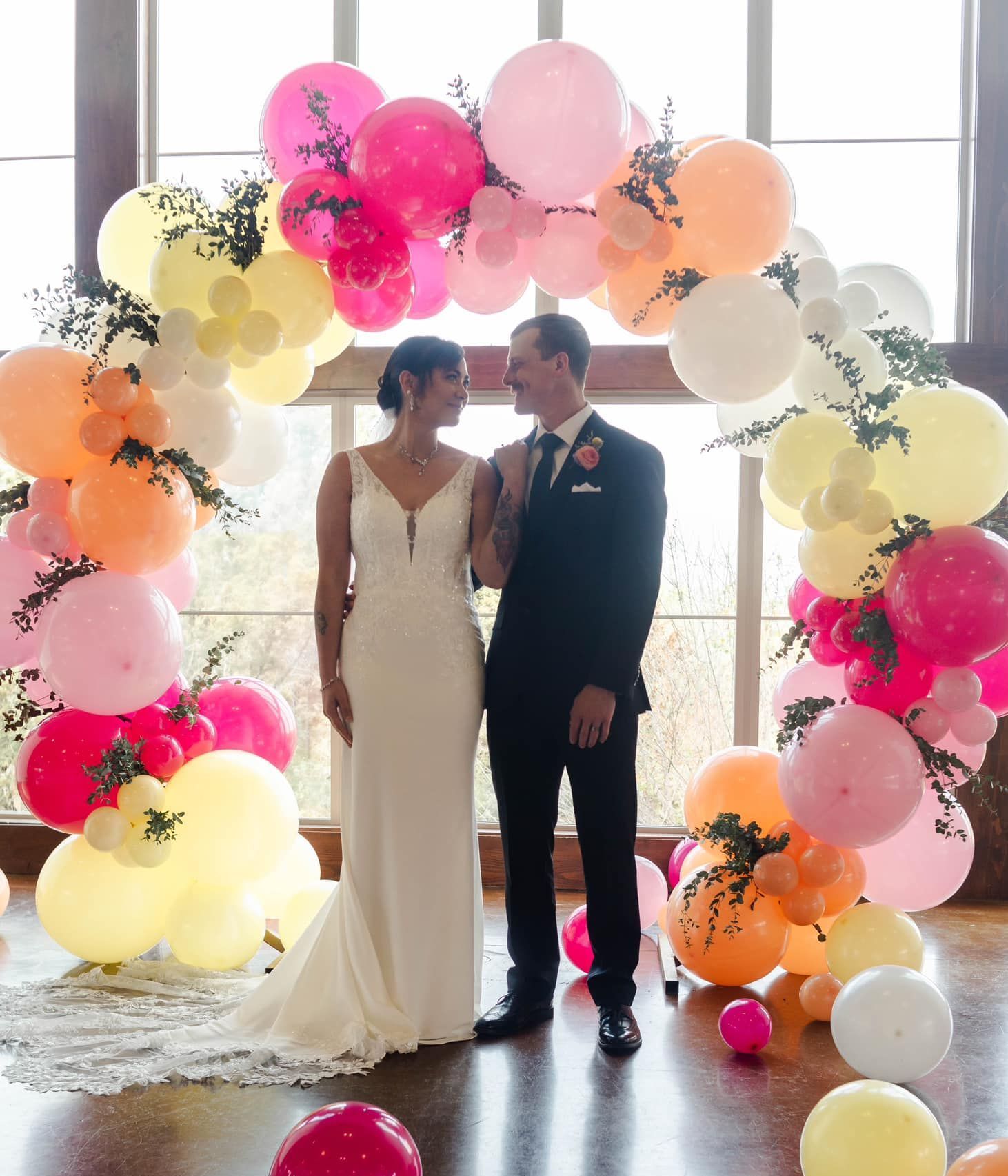 A bride and groom are standing under a balloon arch.
