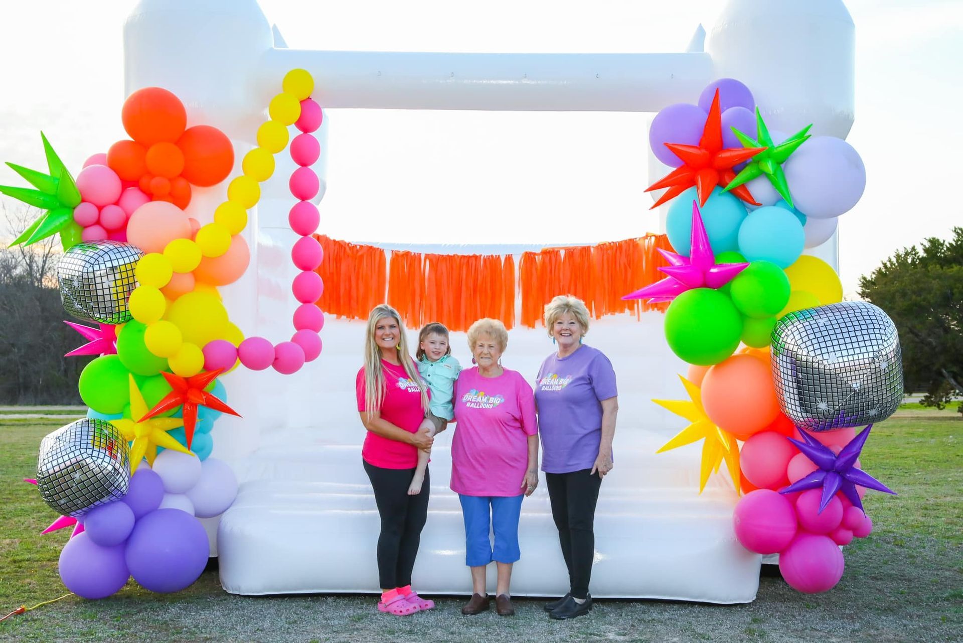 A group of people standing in front of a bouncy house decorated with balloons.