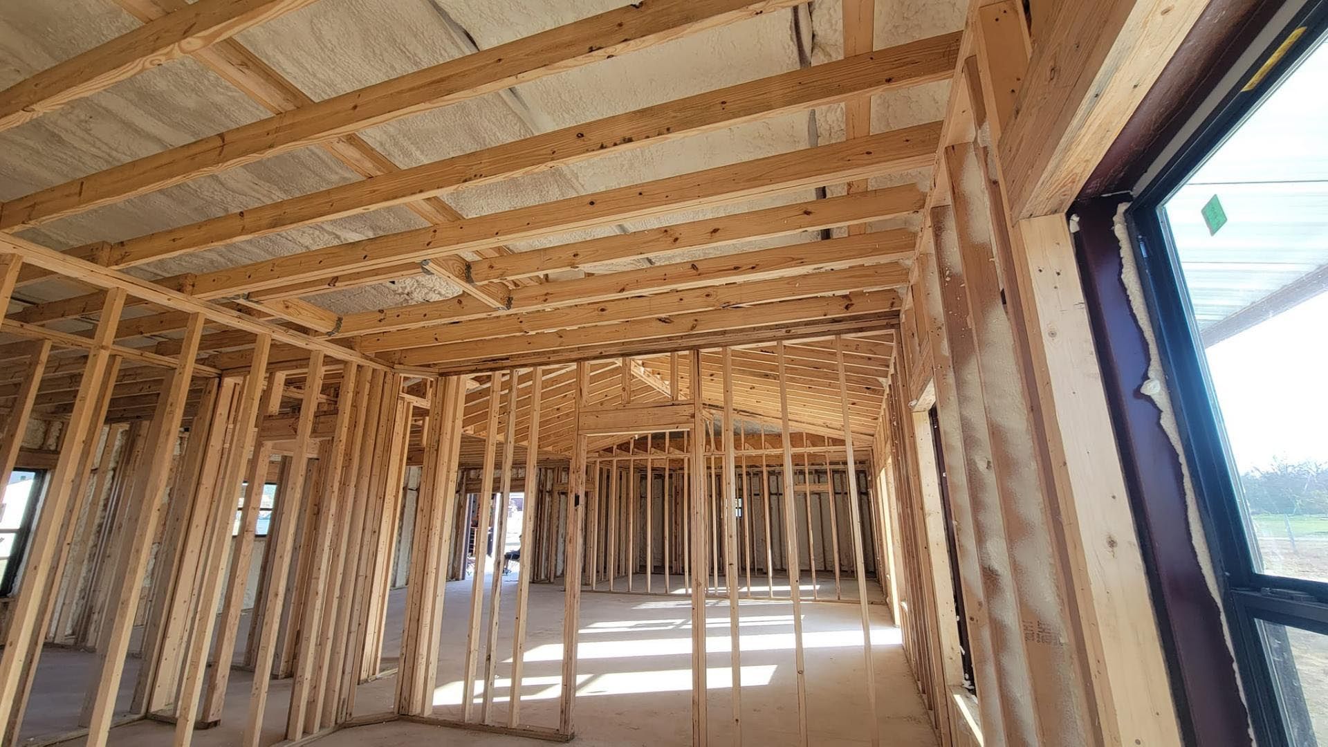 The inside of a house under construction with wooden beams and windows.
