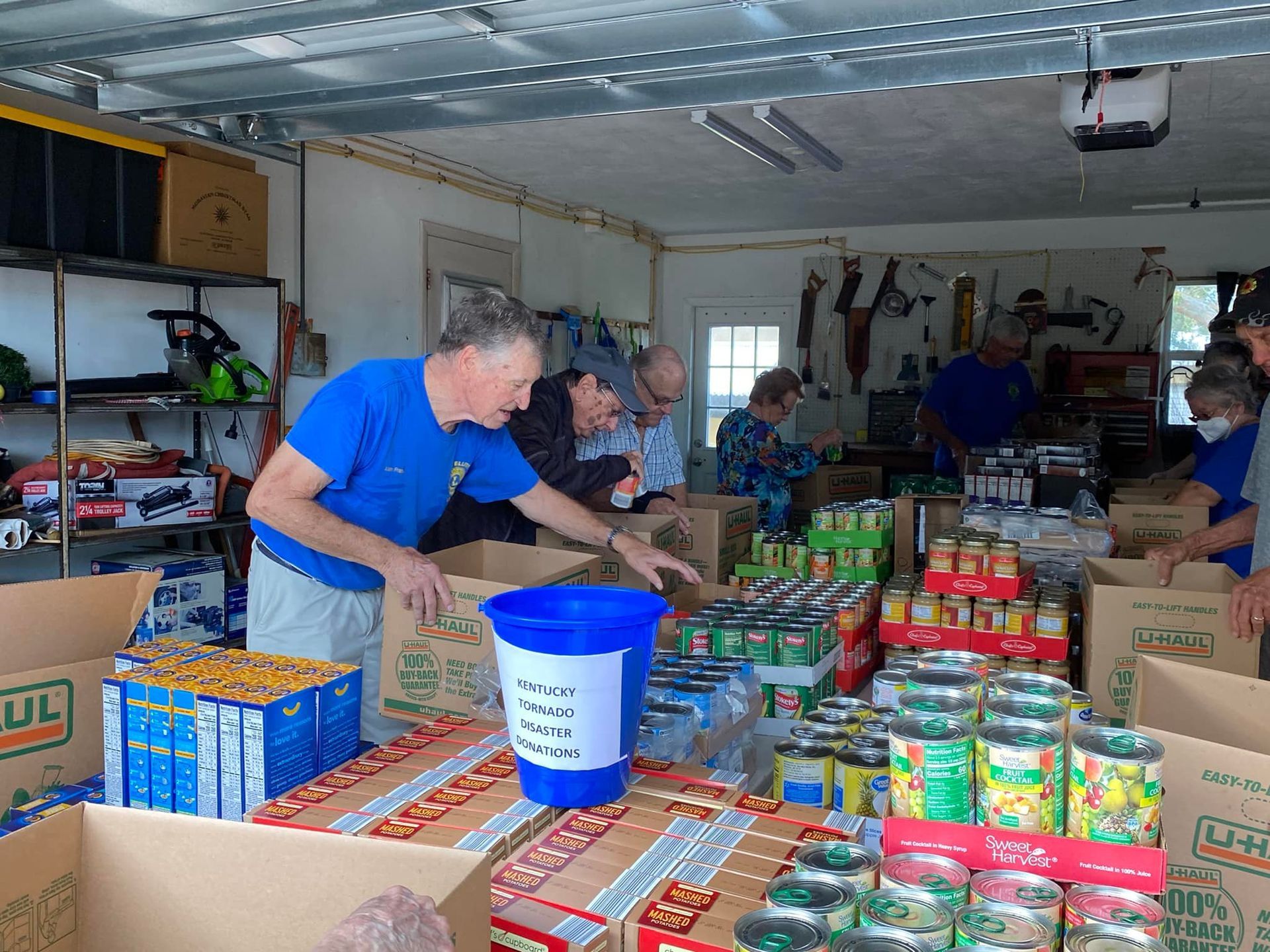 A group of people are working in a garage filled with boxes of food.
