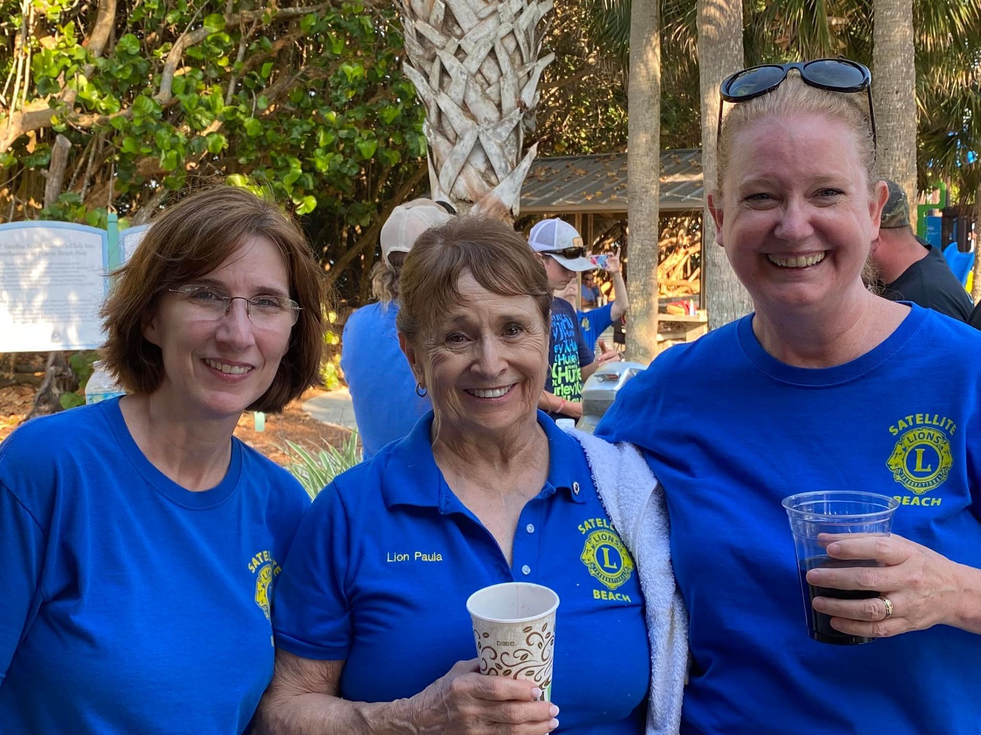 Three women in blue shirts are standing next to each other holding cups.
