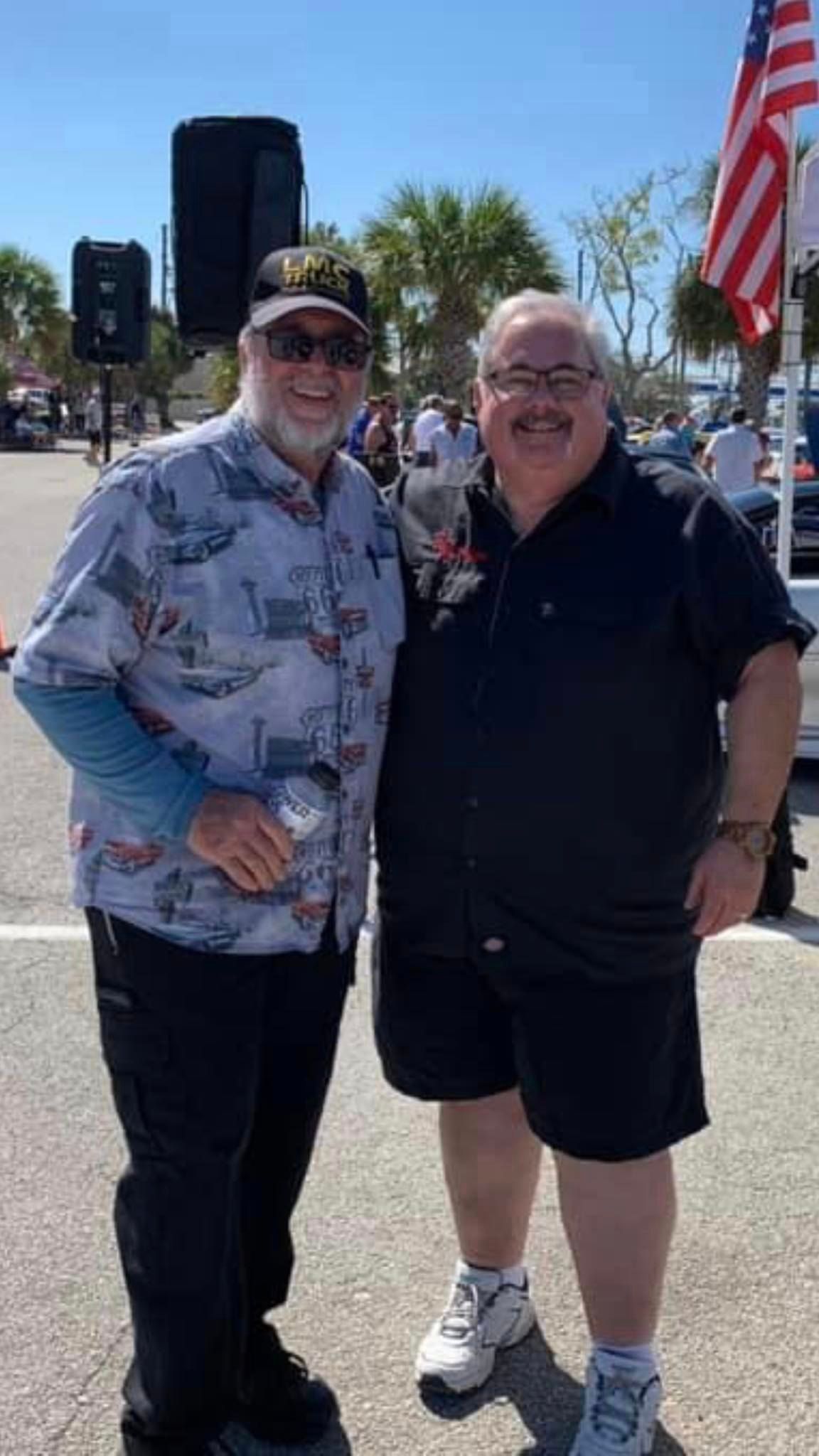 Two men are standing next to each other in a parking lot.