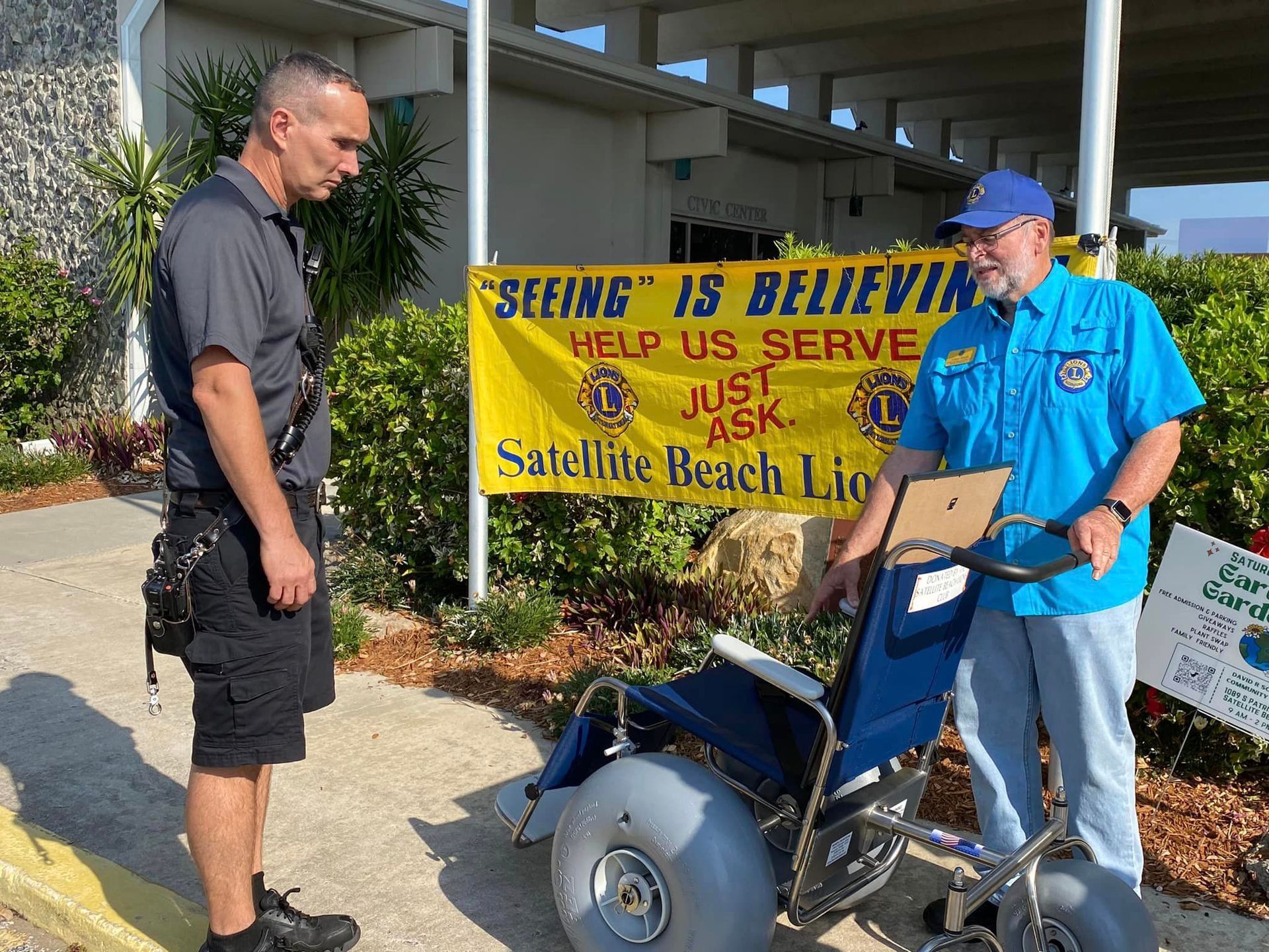 Two men are standing in front of a sign that says seeing is believing