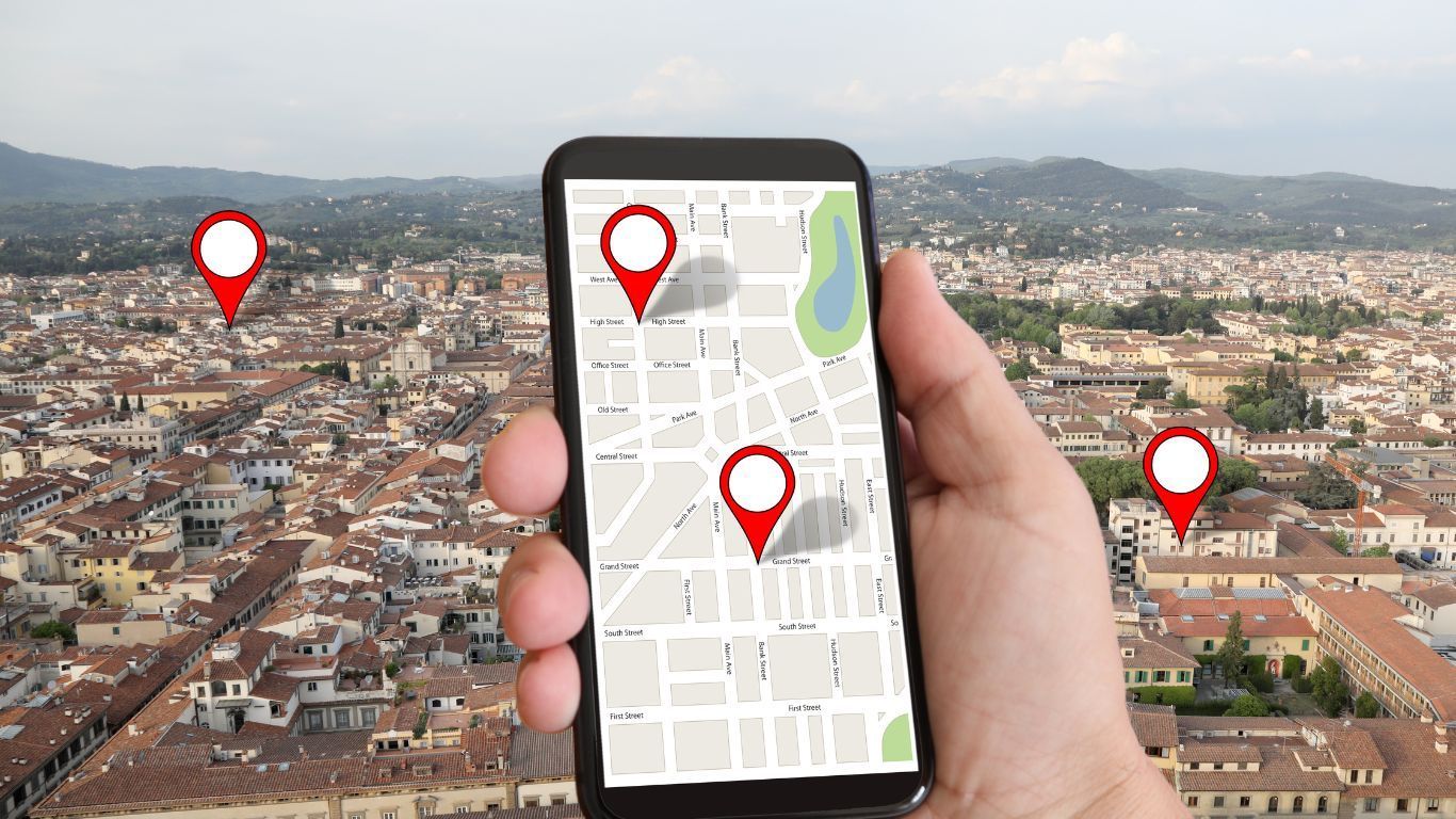 Mão segurando o celular com um mapa e em segundo plano uma cidade
