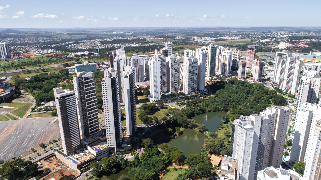 Vista aérea de Goiânia mostrando altos edifícios residenciais modernos ao lado de um lago e vegetação exuberante.