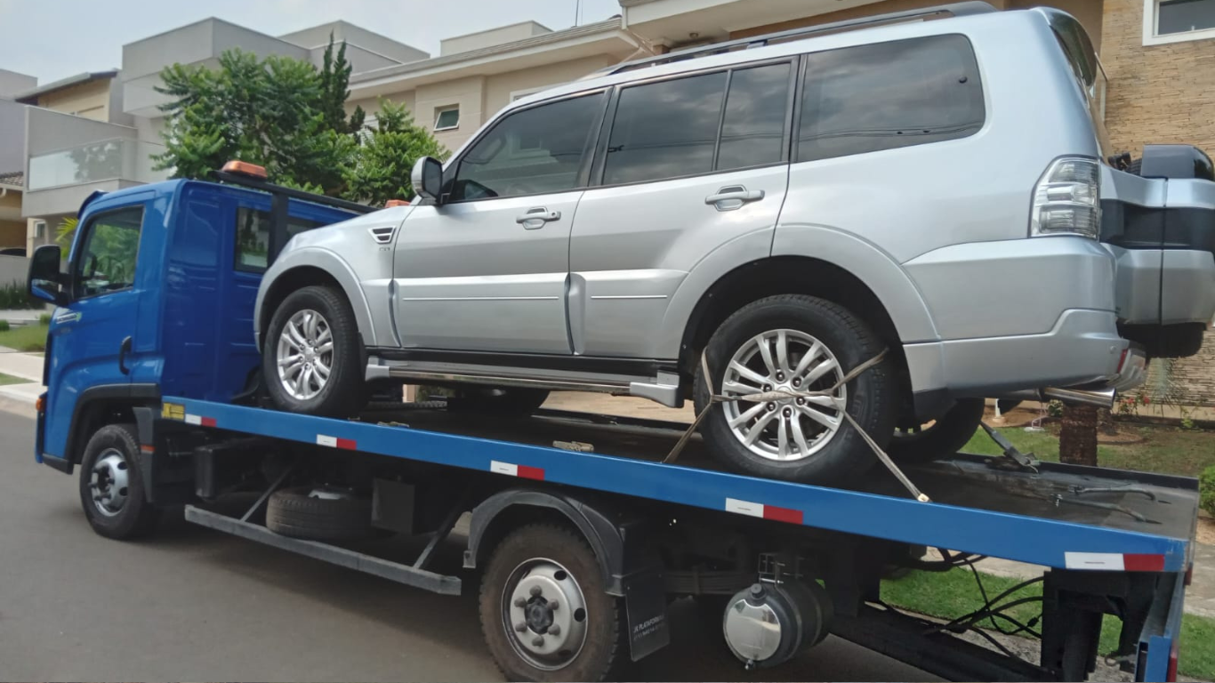 Um SUV prateado é transportado em um guincho azul, seguro e pronto para o transporte.