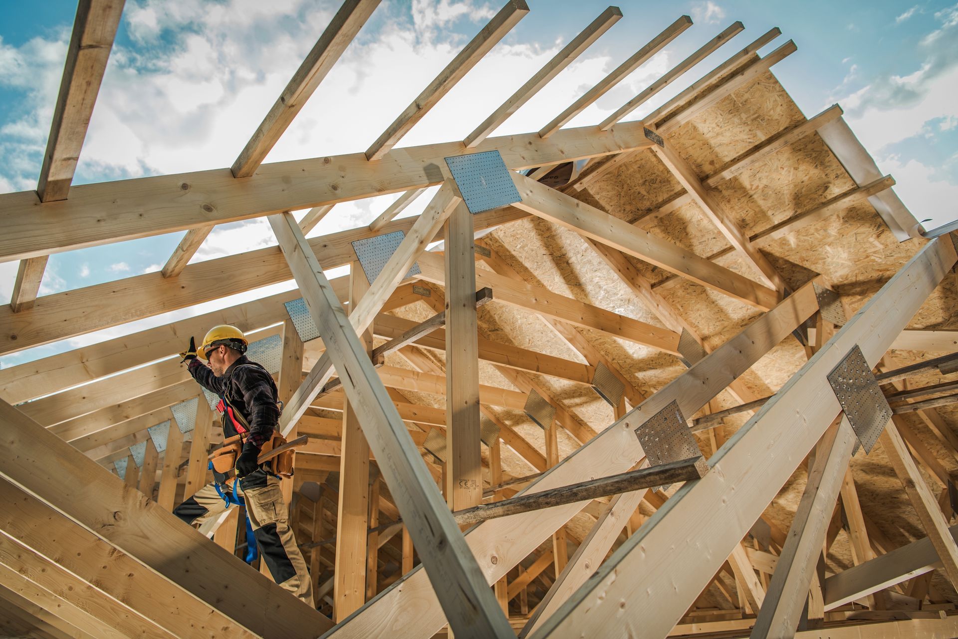 Un ouvrier du bâtiment, perché sur une charpente de toit en bois, portant un casque et un équipement de sécurité