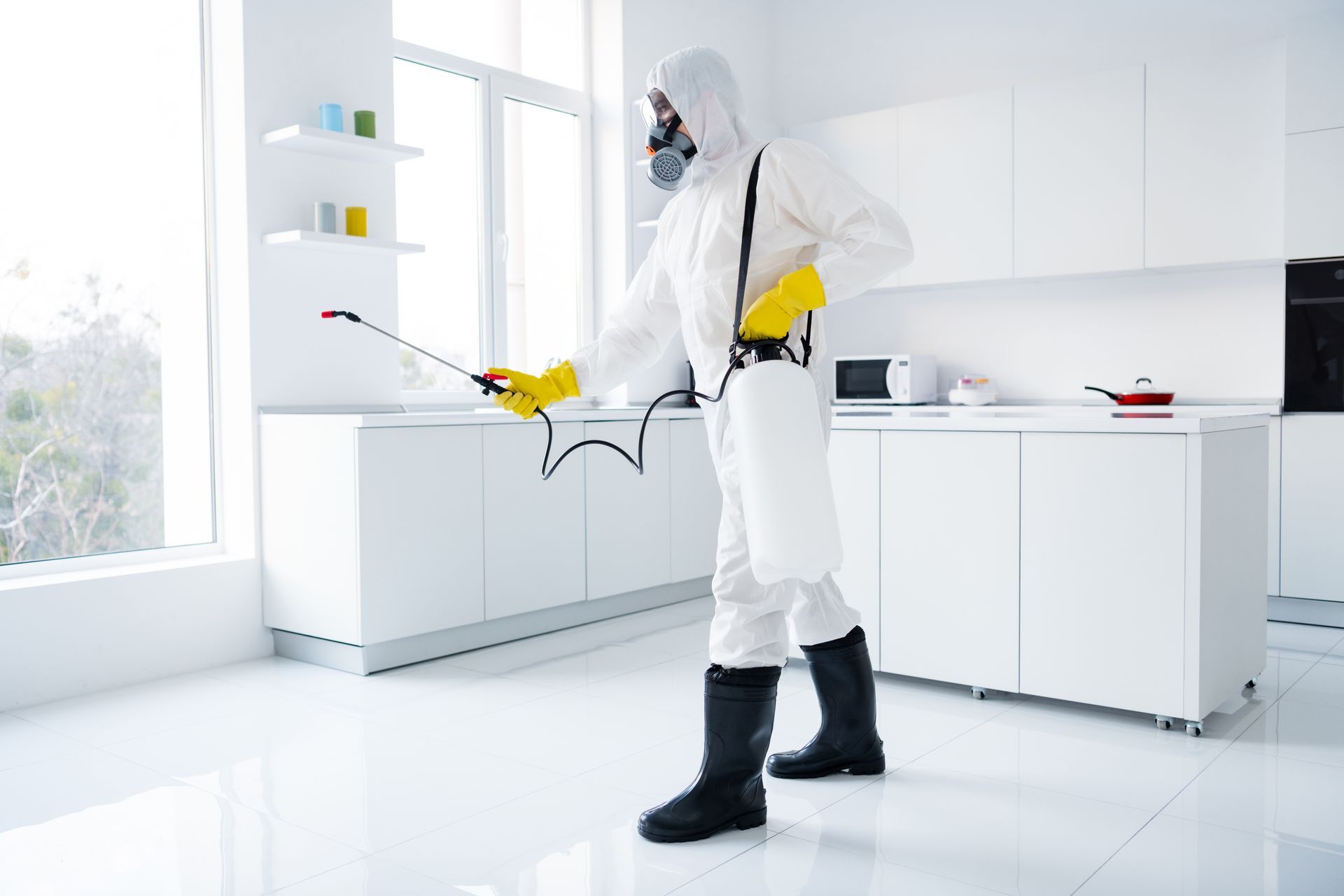 Technician in protective gear treating a kitchen for effective and safe pest control services.