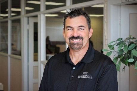 Man with dark hair and goatee in black polo shirt smiles indoors.