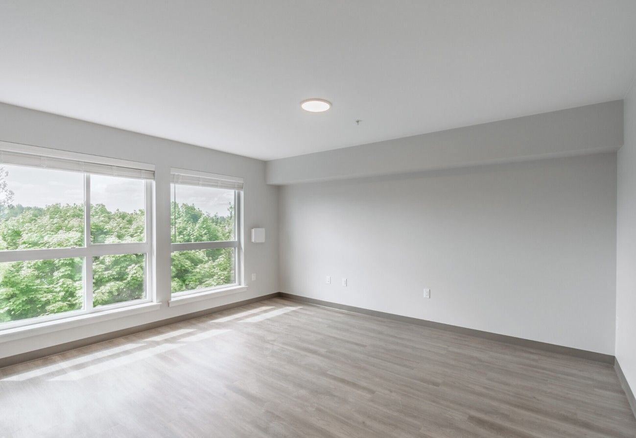An empty living room with hardwood floors and two windows.