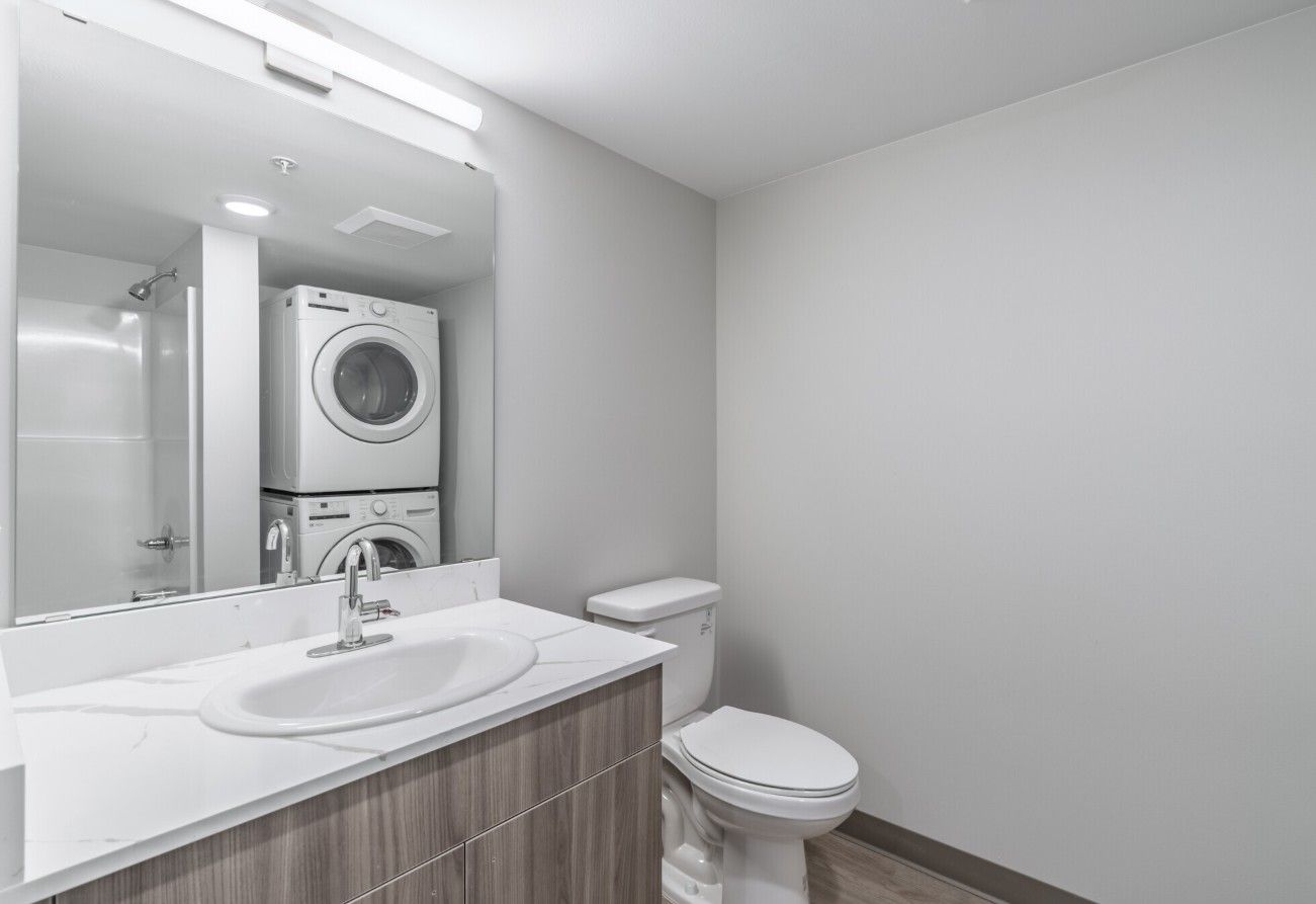 A bathroom with a sink , toilet , washer and dryer stacked on top of each other.