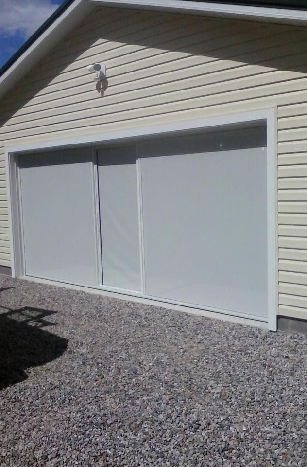 White garage door, closed, with light-colored siding, set in gravel driveway.
