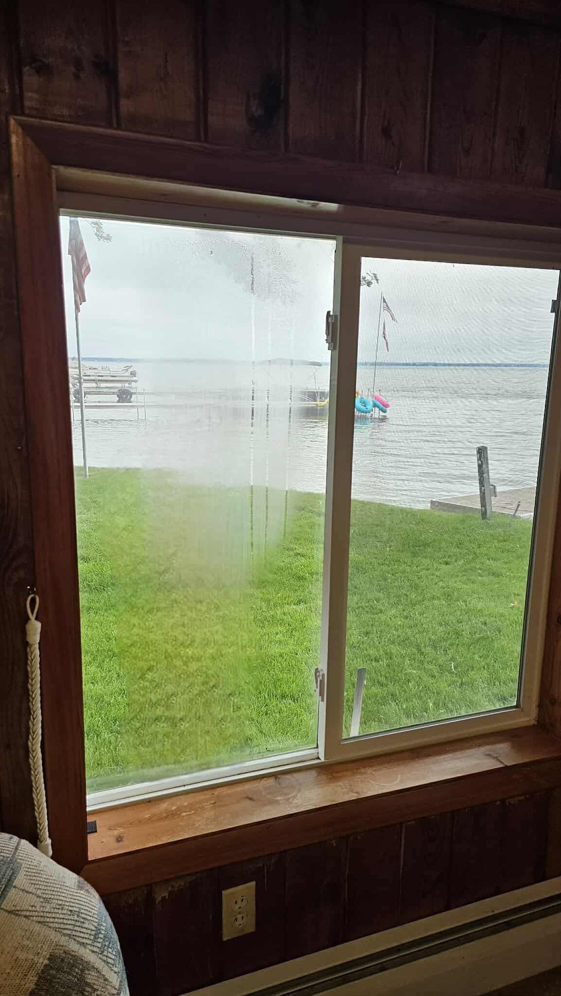 Window view of lake and green grass, boats in water, overcast day.