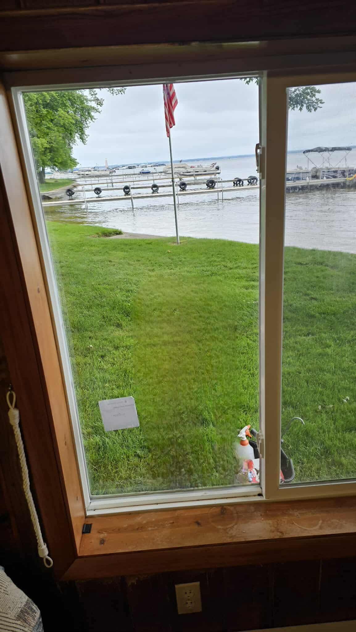 View from a window overlooking a green lawn, water, and docked boats under a cloudy sky.