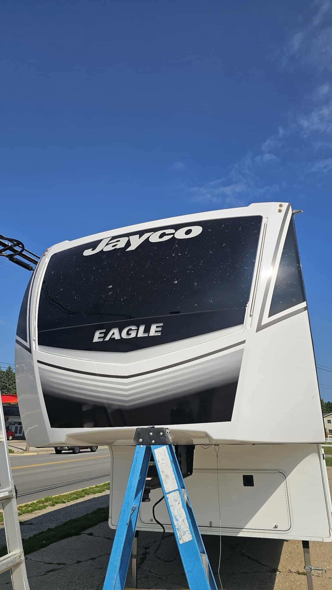 Jayco Eagle RV with a black front panel, parked under a blue sky, supported by a blue ladder.