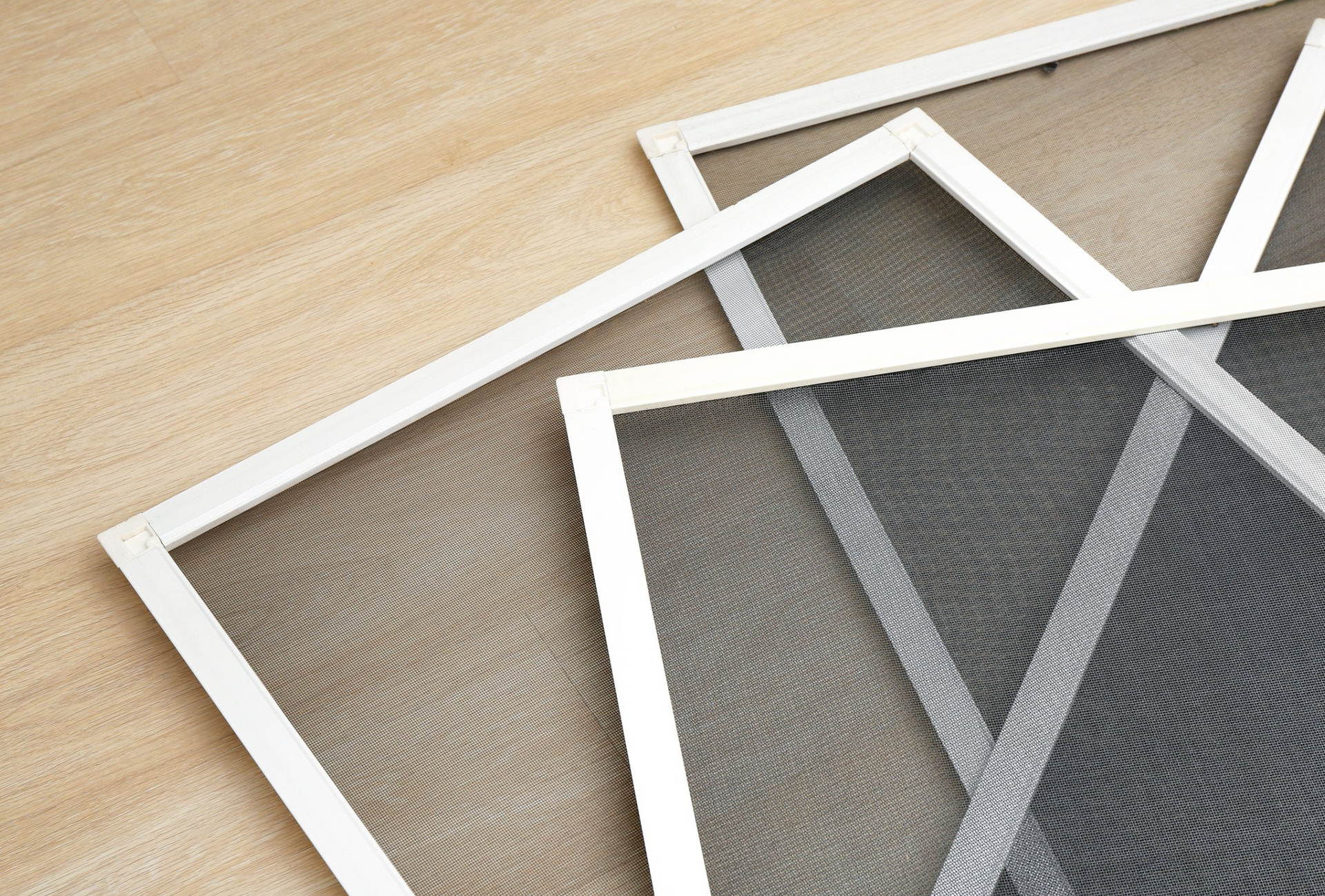 Close-up of three window screens with white frames, lying on light wood surface.