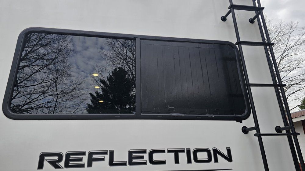 RV window with black trim and shade, ladder, and 