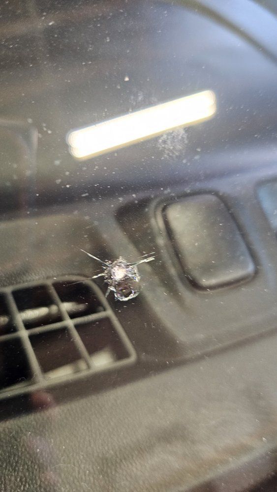 Windshield with a star-shaped crack from impact, near dashboard air vent.