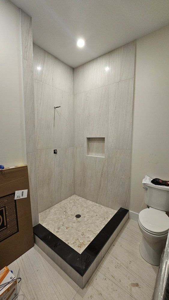 New, tiled shower with a step-up base and a toilet to the right.