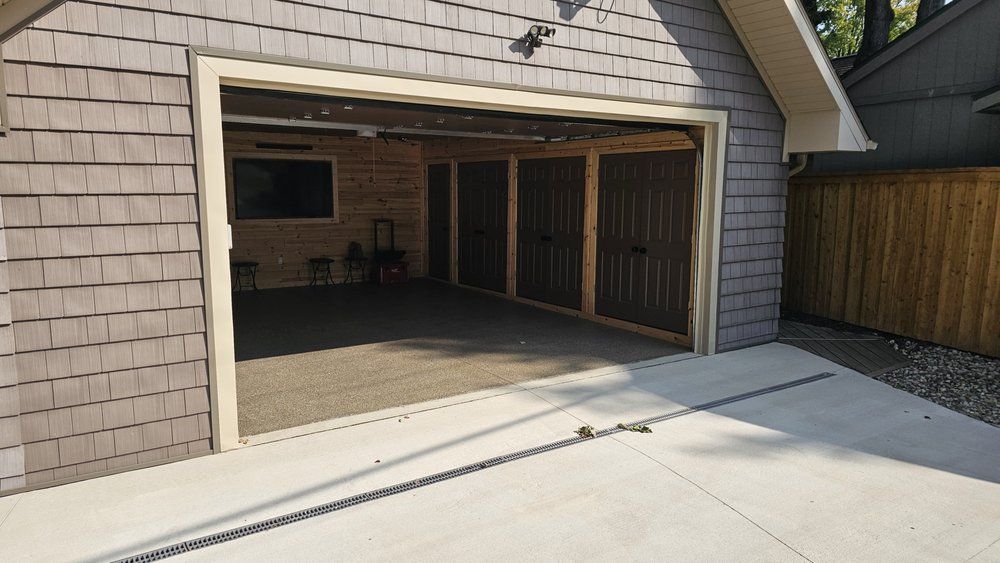 Garage exterior with open door, gravel floor, and brown storage doors.