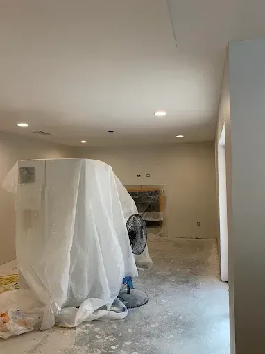 A room with a fan and a white sheet on the floor.