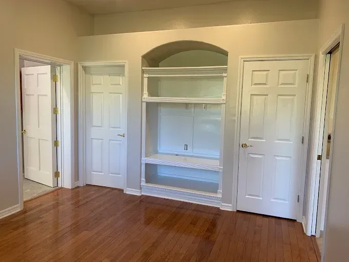 An empty room with hardwood floors , white doors and shelves.