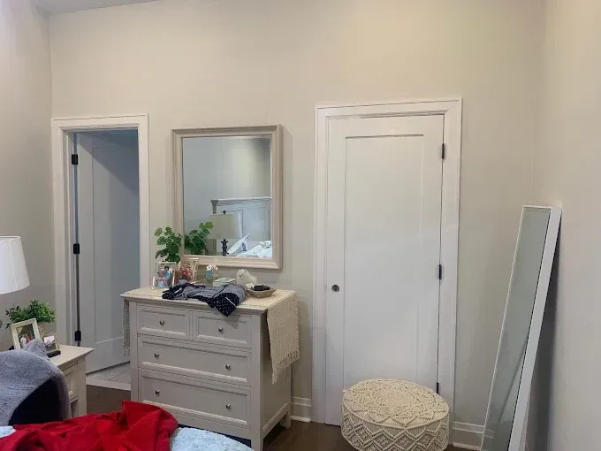 A bedroom with a bed , dresser , mirror and ottoman.