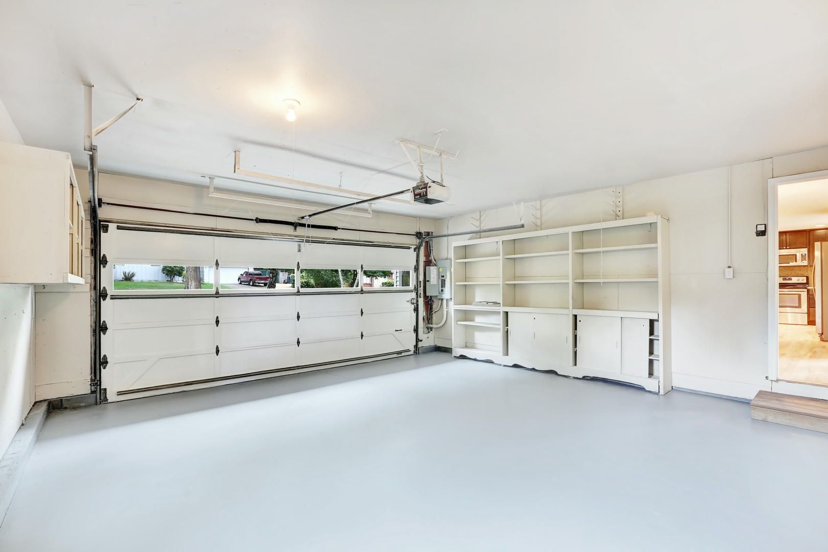 An empty garage with a garage door open and shelves.