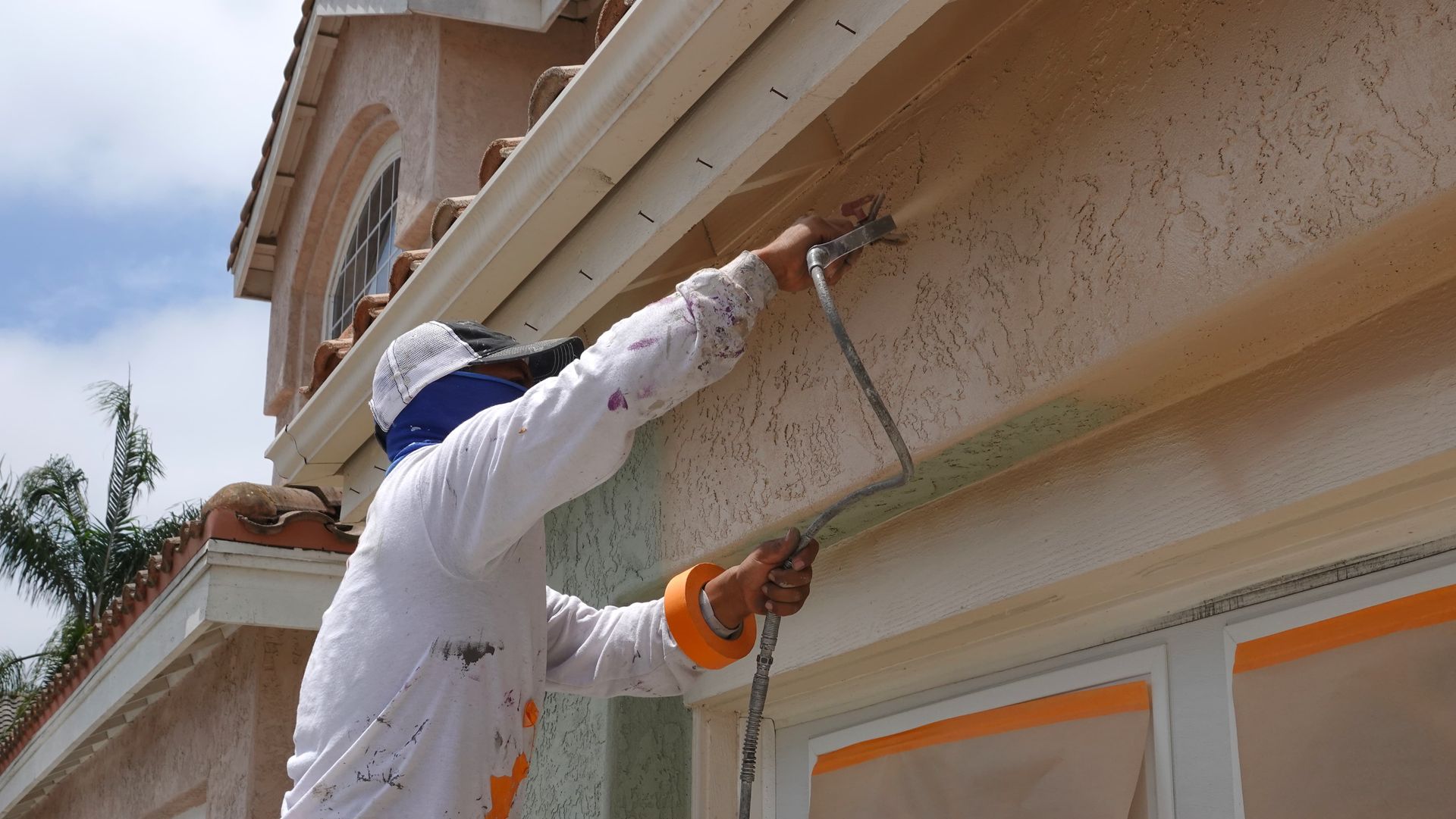 A man is spray painting the side of a house.