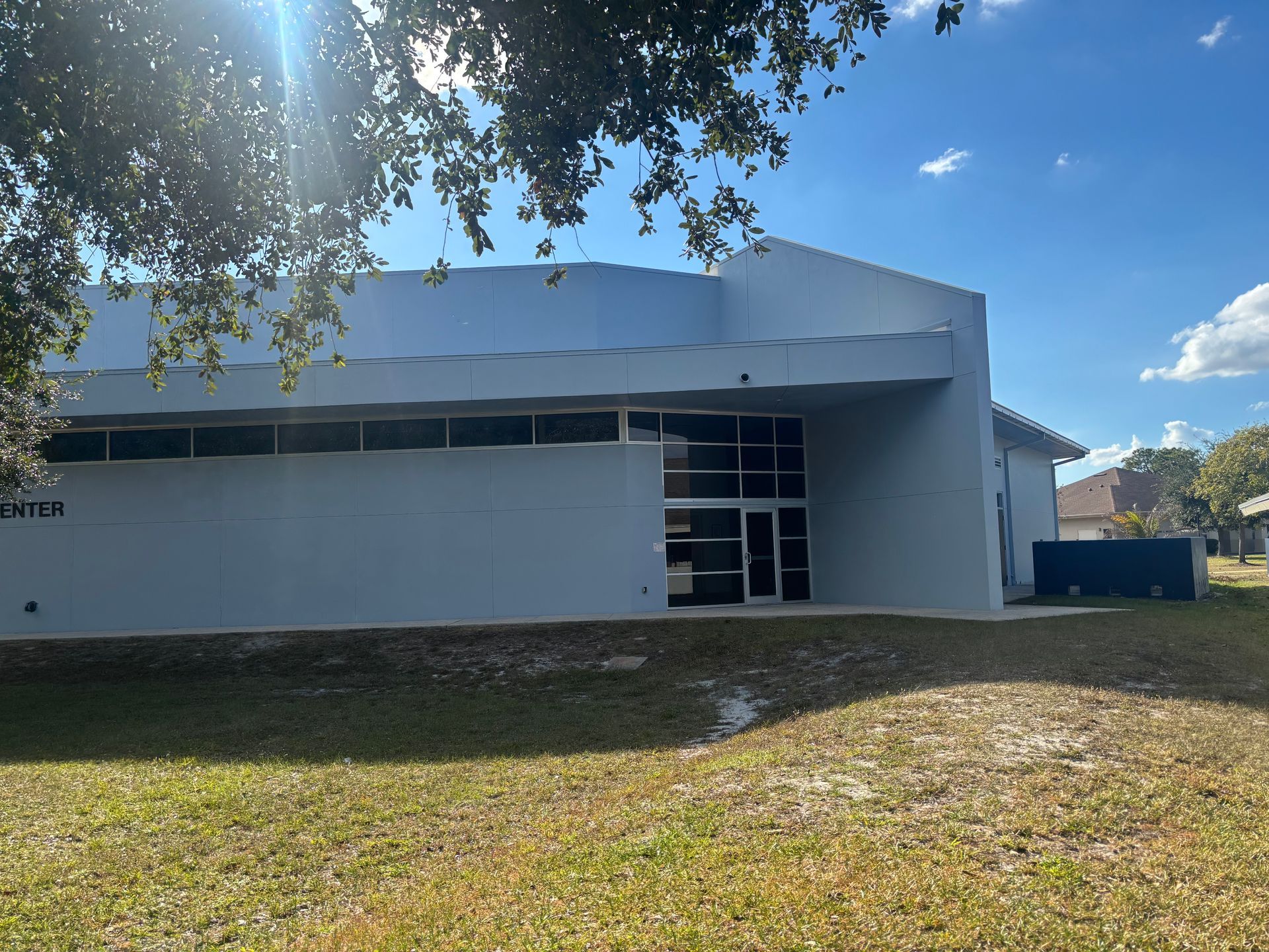 Blue building with large windows and a curved roof, on a grassy lot under a sunny sky.