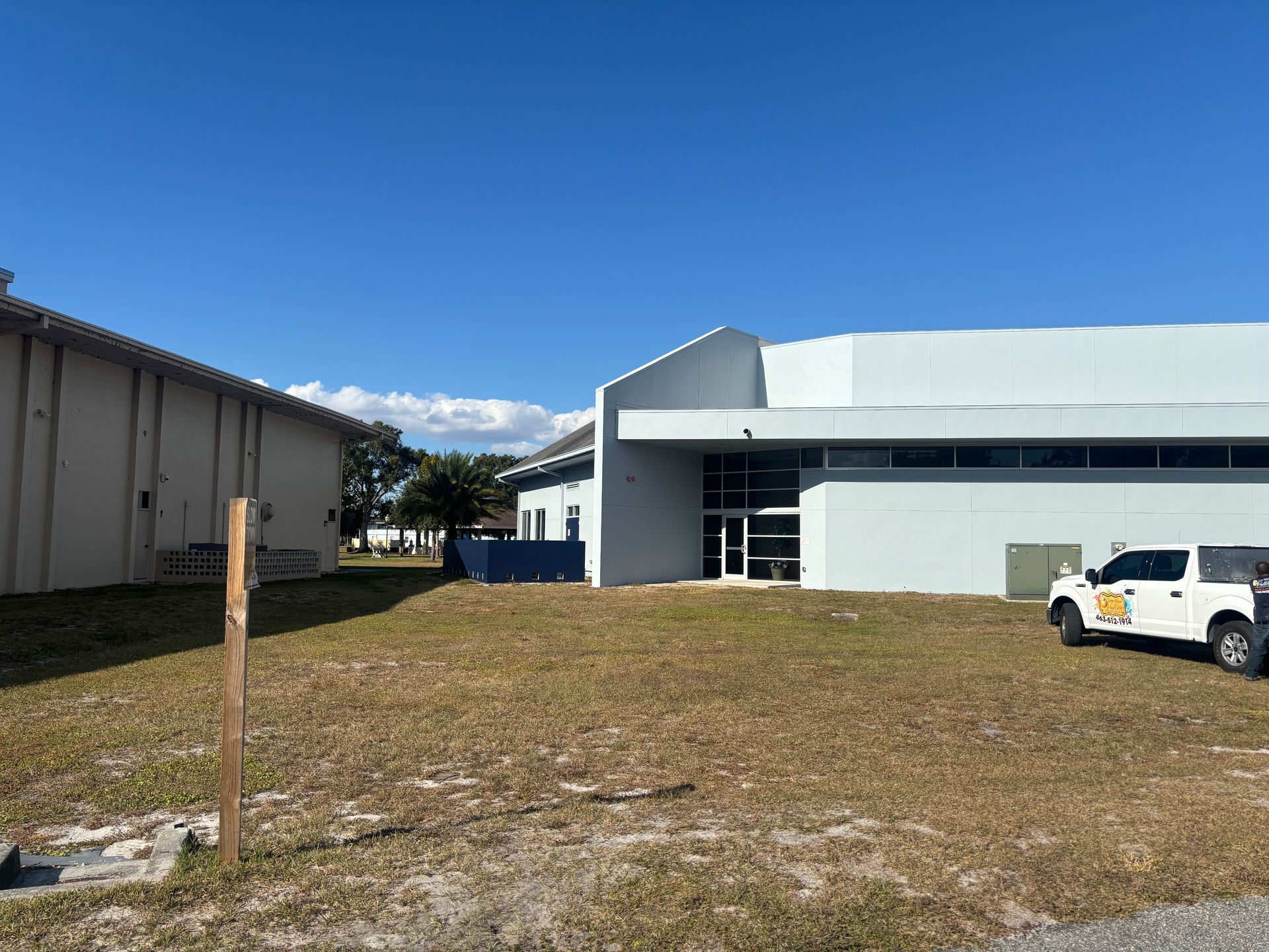 Two light blue buildings on a grassy field under a clear blue sky. A white truck is parked nearby.