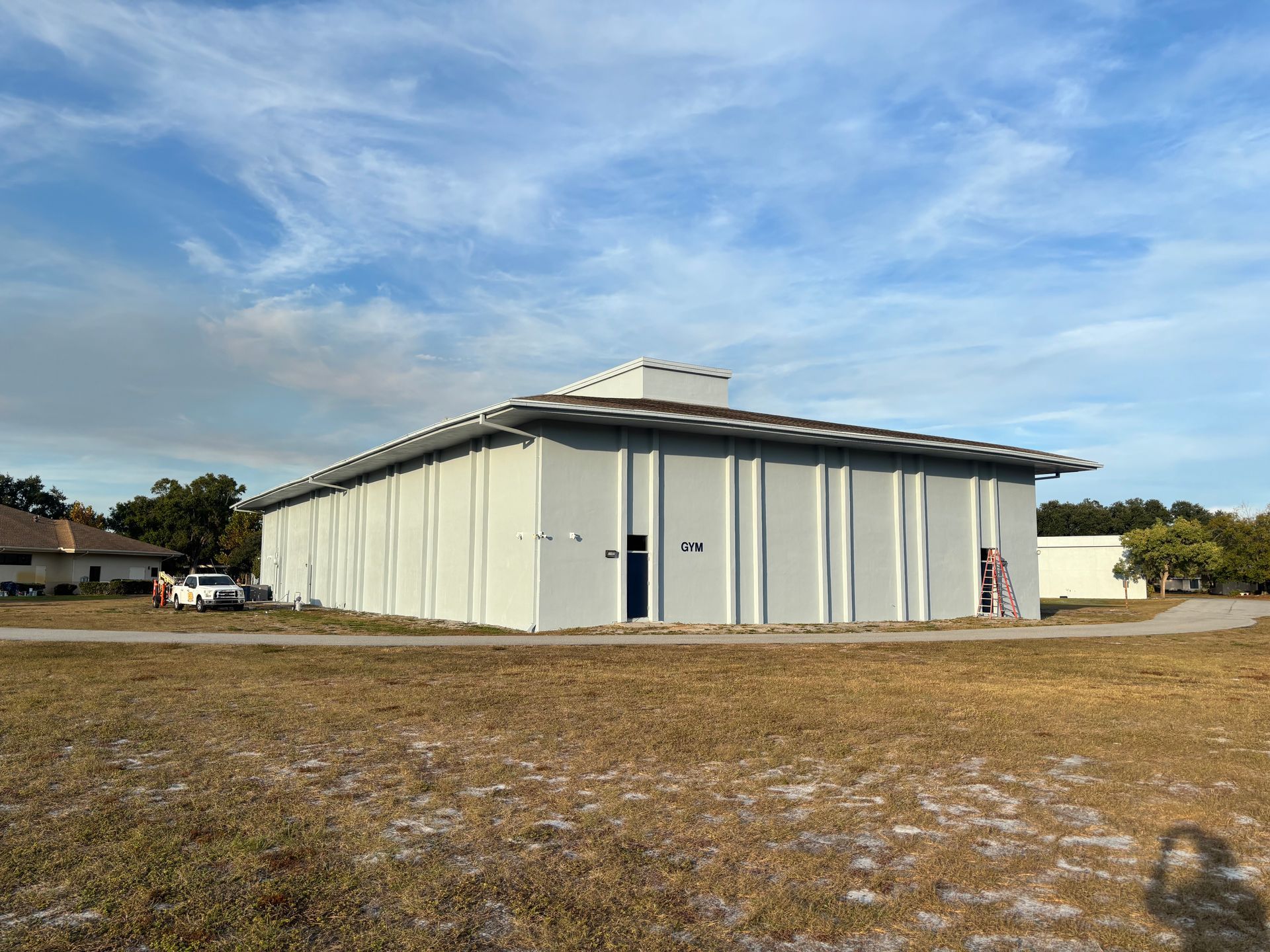 Gray building with vertical lines, surrounded by brown grass under a blue sky.