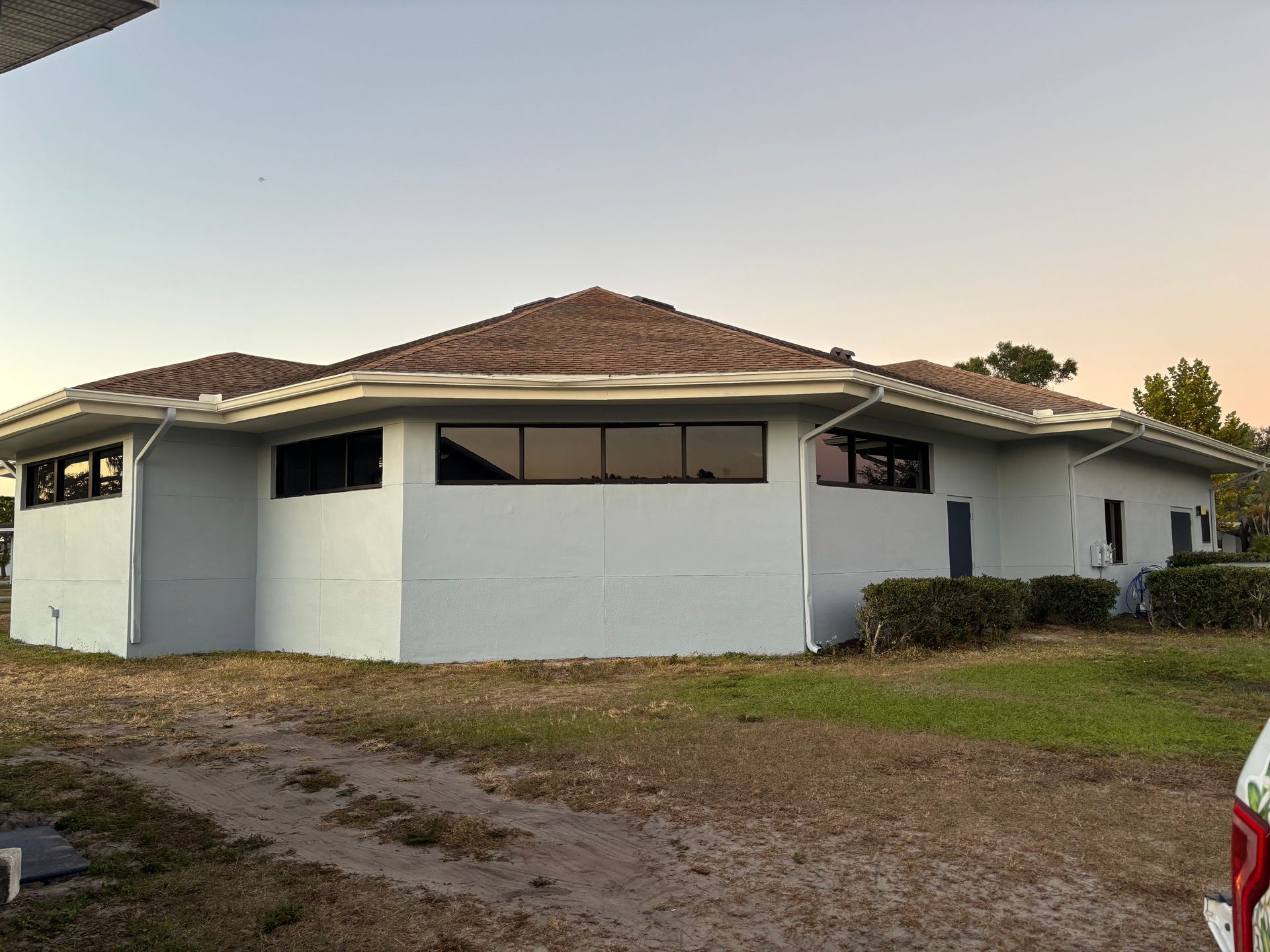 Light blue building with brown roof, several windows, and dry grass.
