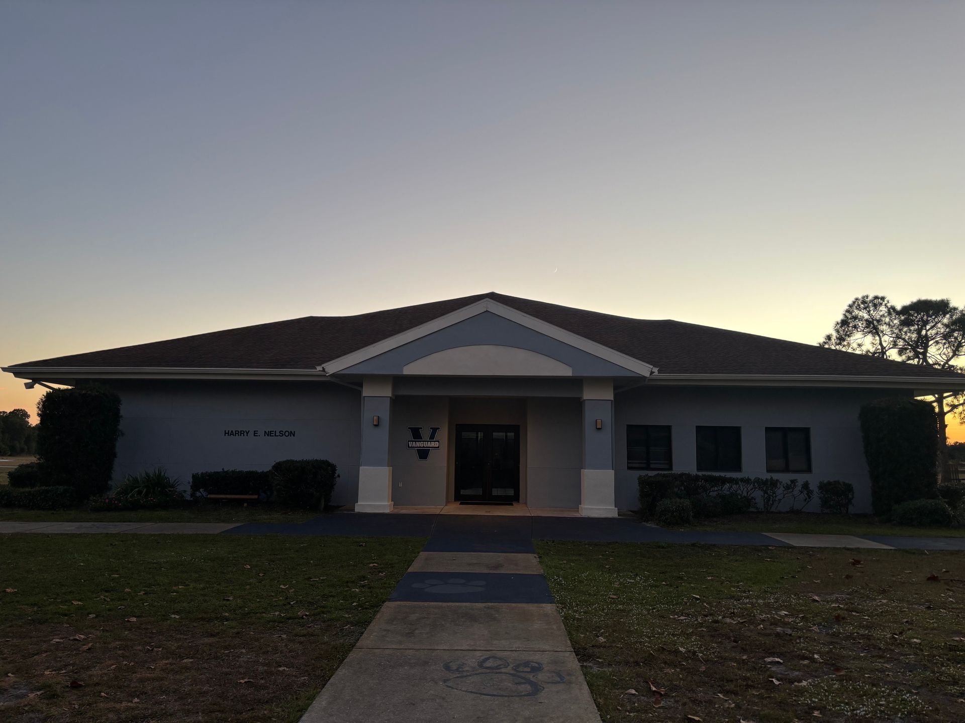 A one-story building with a brown roof and a walkway leading to the entrance; dusk sky.