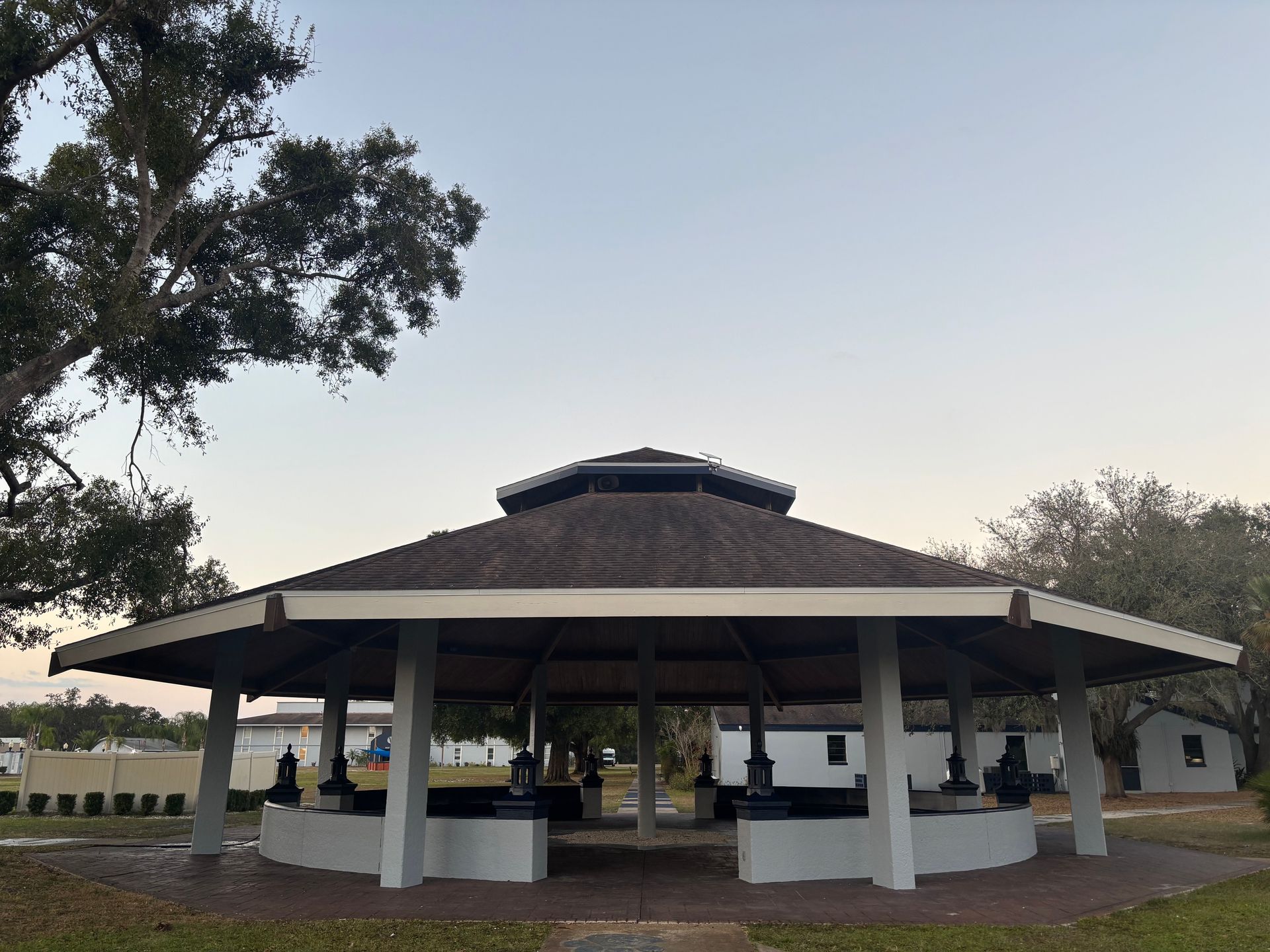 A gazebo with dark statues beneath its roof, on a grassy area under a partly cloudy sky.