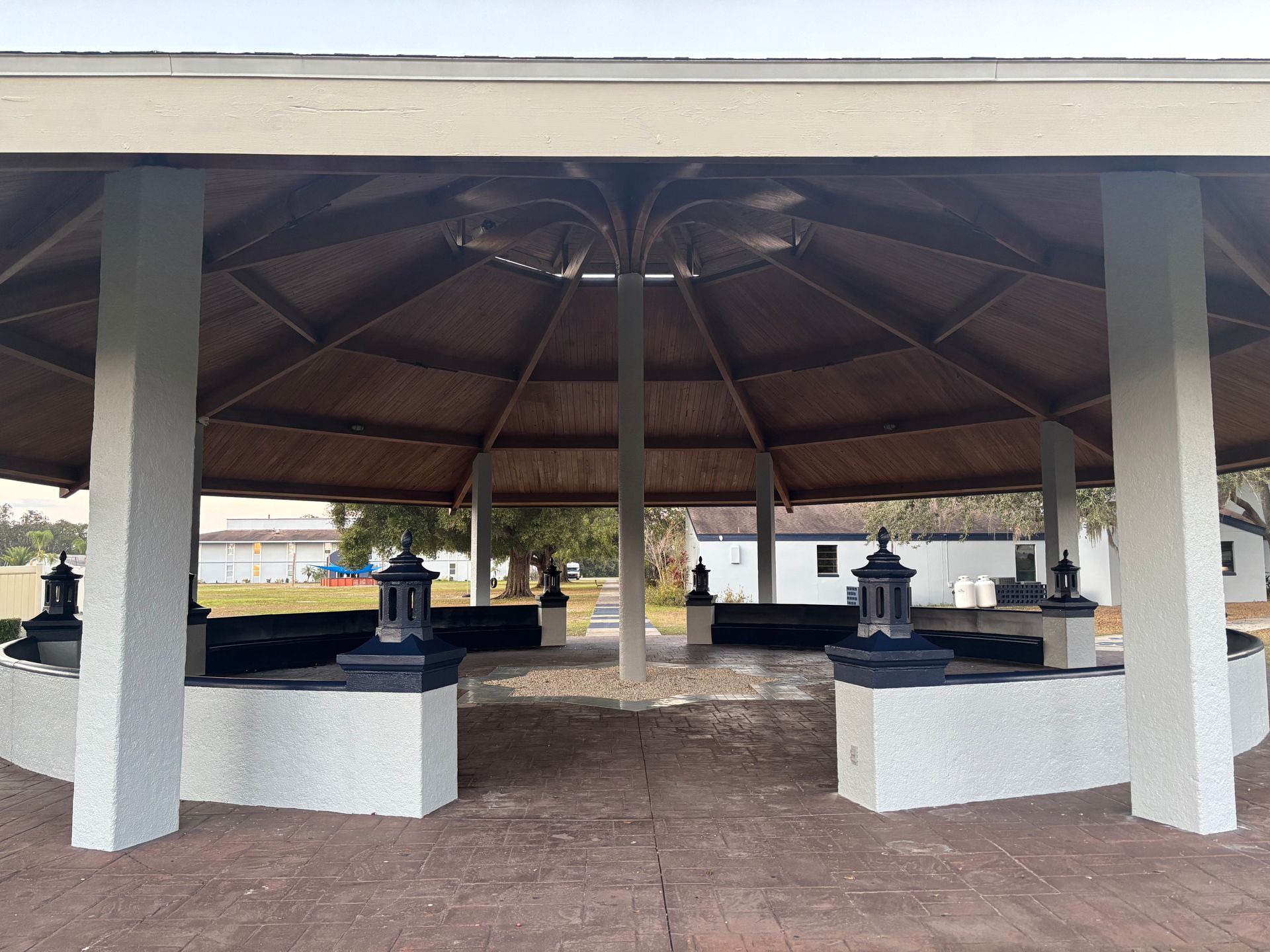 Gazebo with concrete pillars, dark roof, benches, and outdoor lamps.